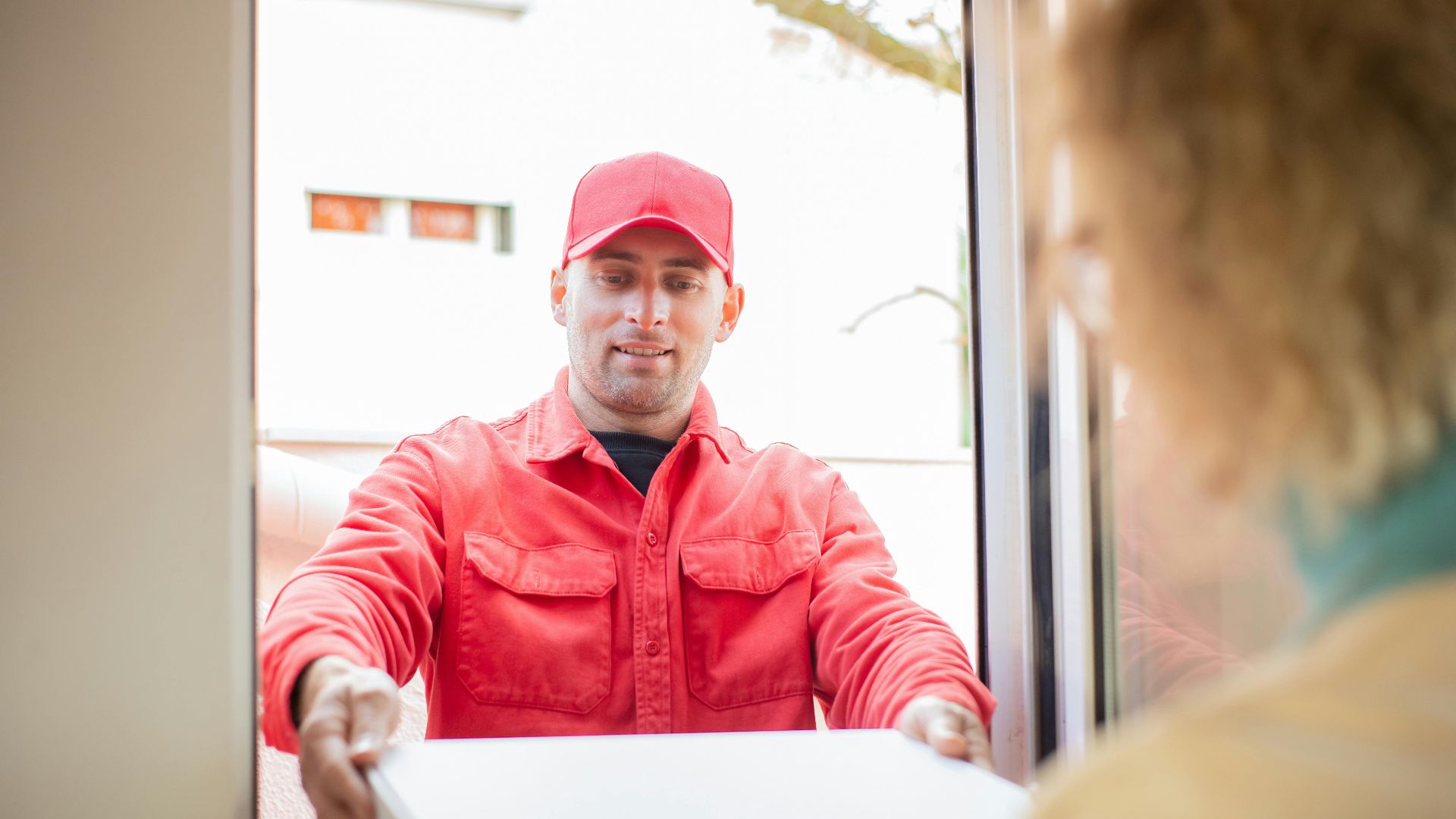 A delivery person in red uniform handing over a package at a doorway.
