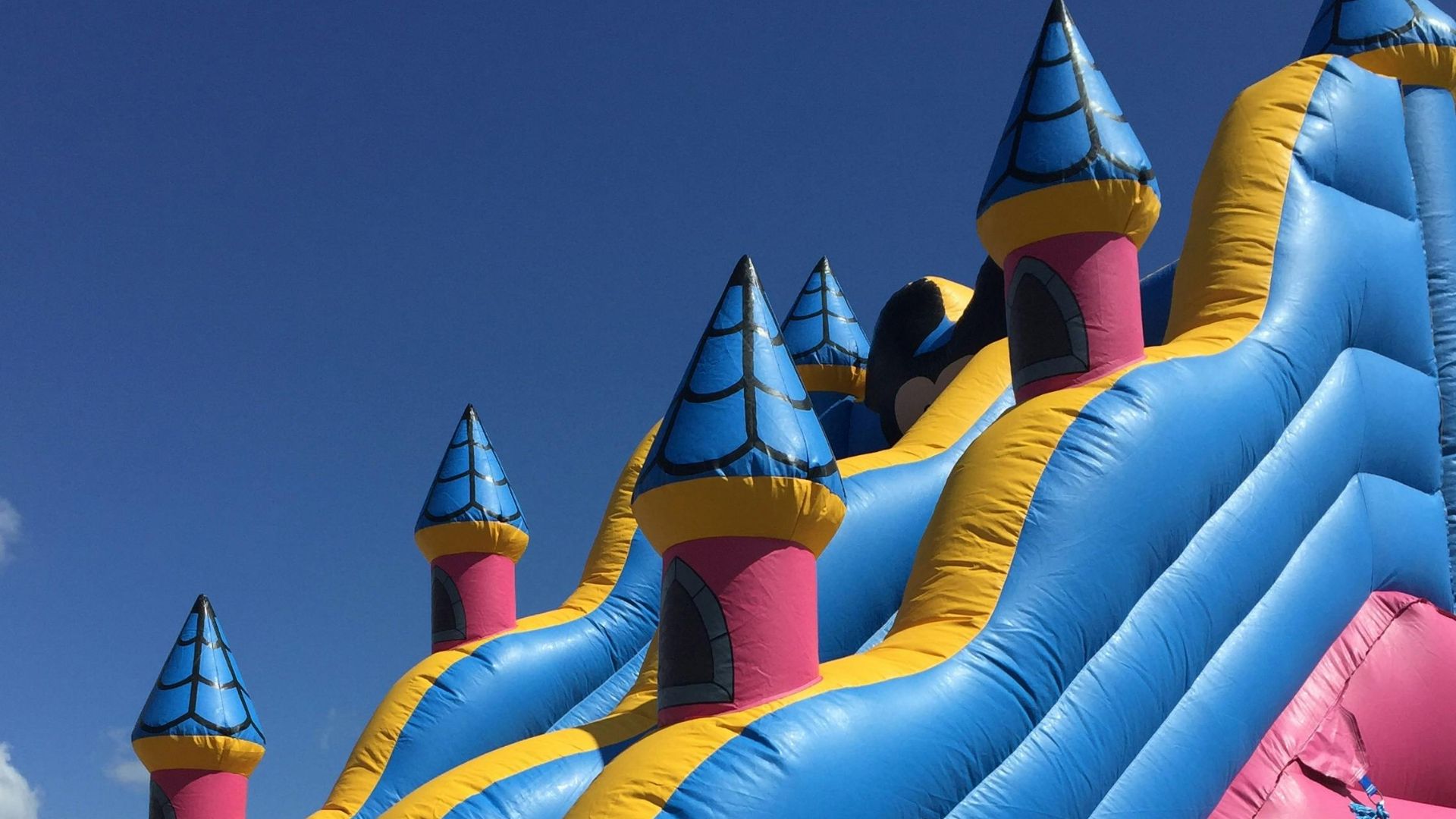 Bright inflatable slide with colorful turrets against a clear blue sky. Fun and playful atmosphere.