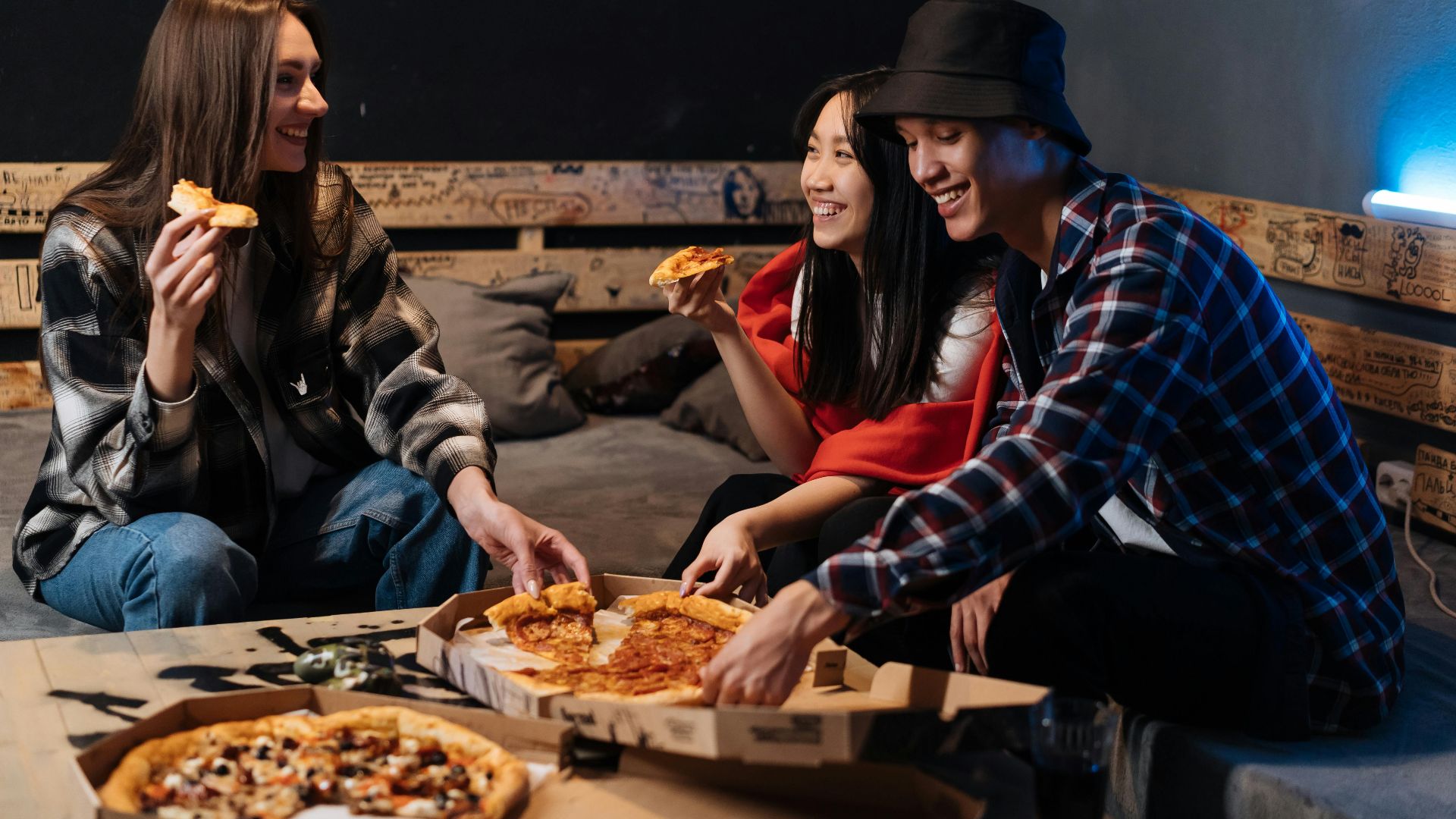 Group of friends enjoying pizza and laughter indoors, creating fond memories.