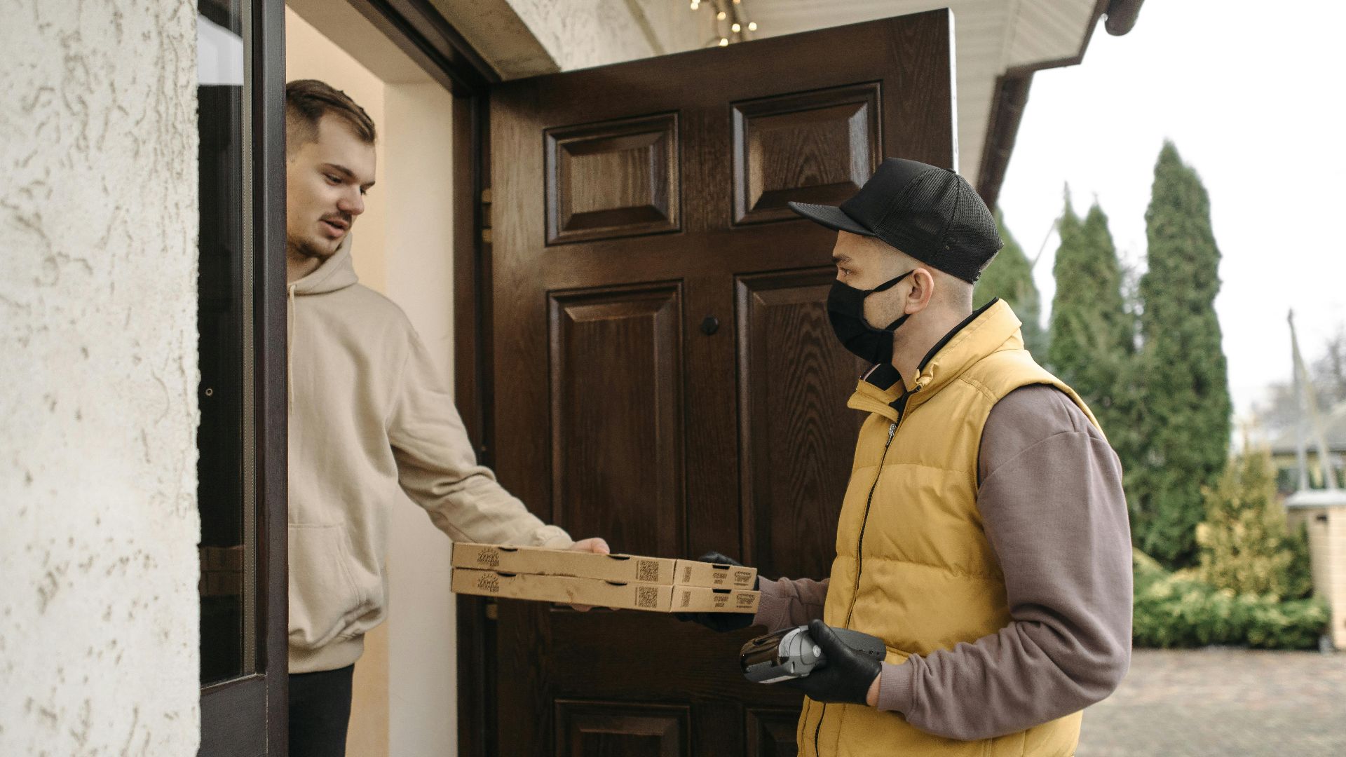 Courier delivering pizza boxes at the doorstep using contactless payment method.
