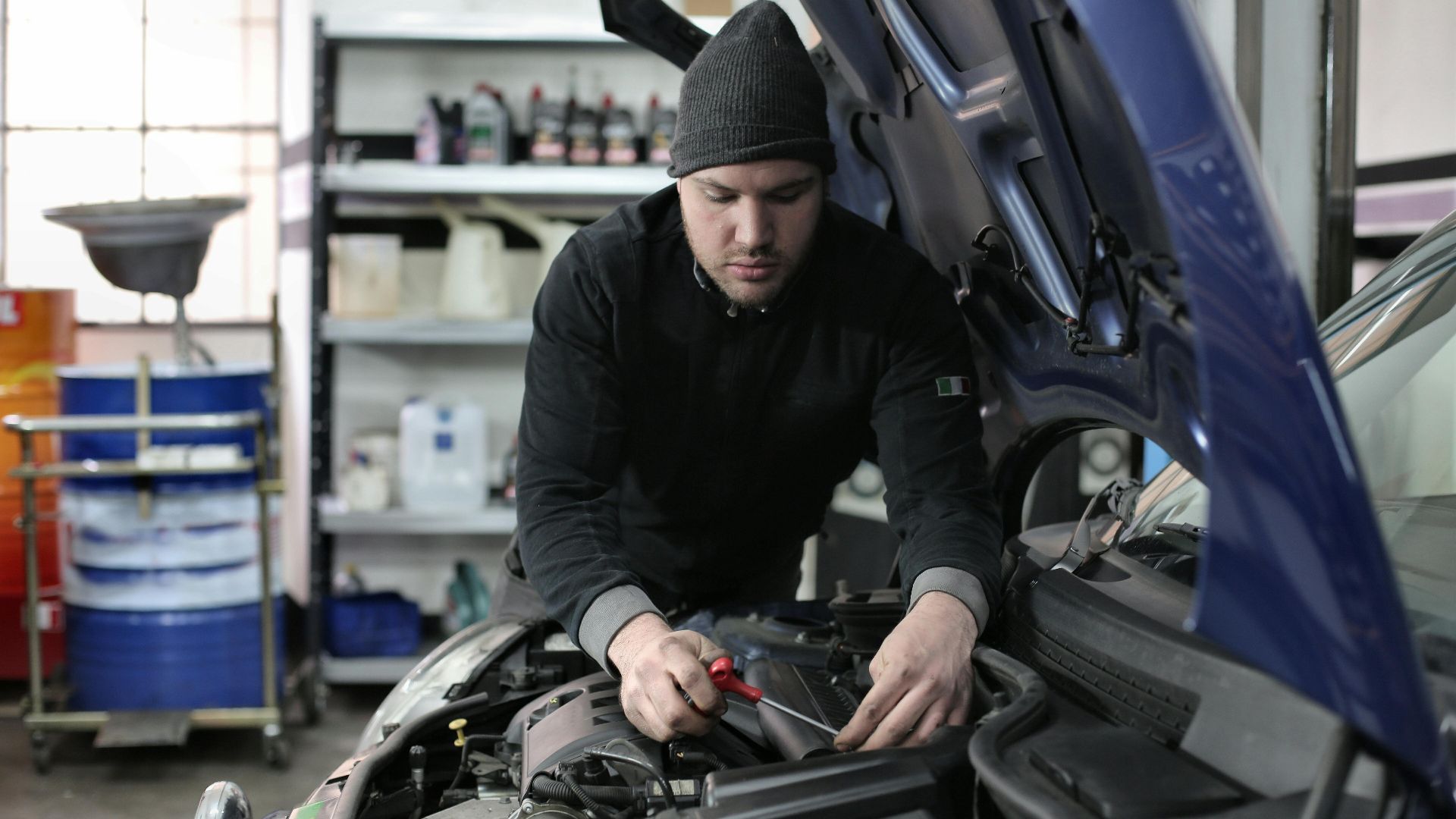 Man working under car hood in a garage, focused on engine repair