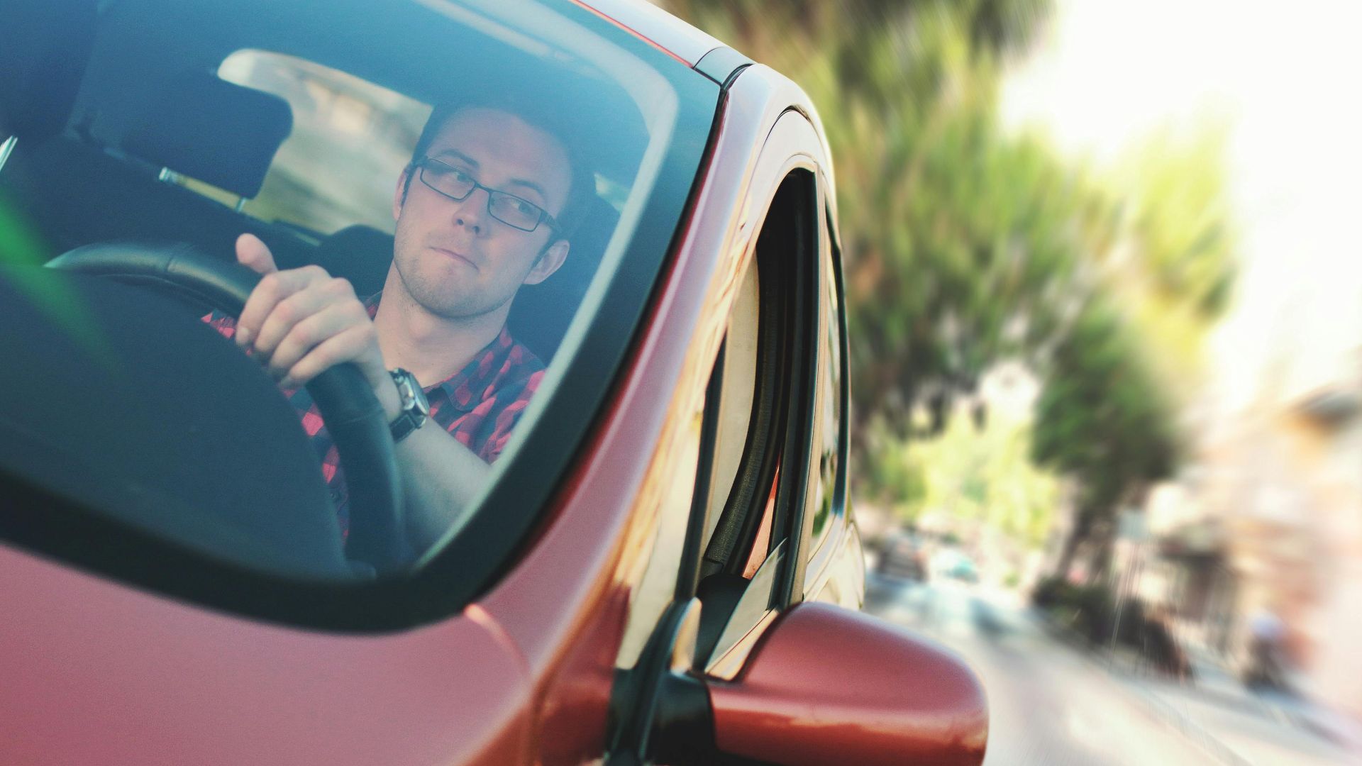 A man driving fast through a city street in a red car, showcasing motion and focus.