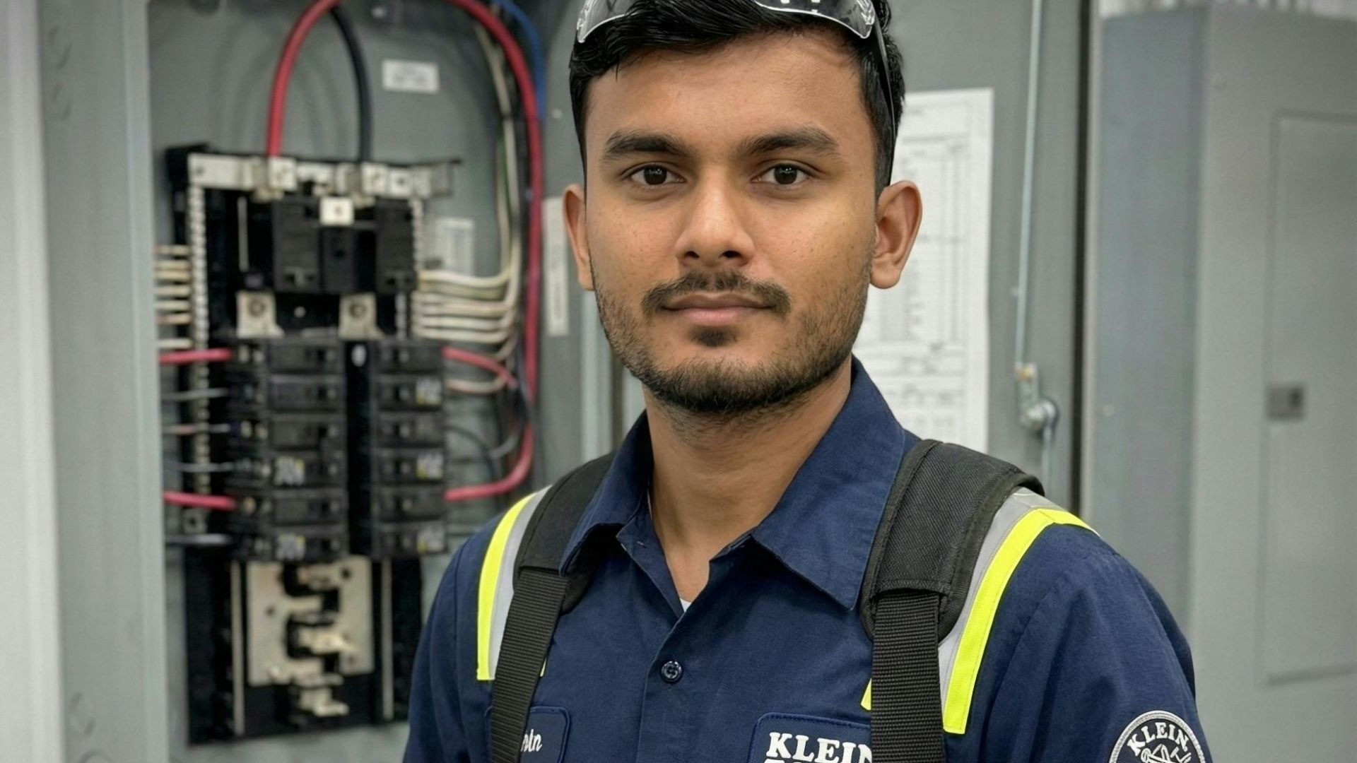 Electrician in safety gear inspecting circuit breakers with a meter.
