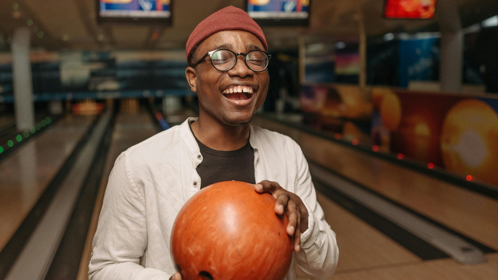 Happy man at a bowling alley, holding a ball and smiling joyfully indoors.