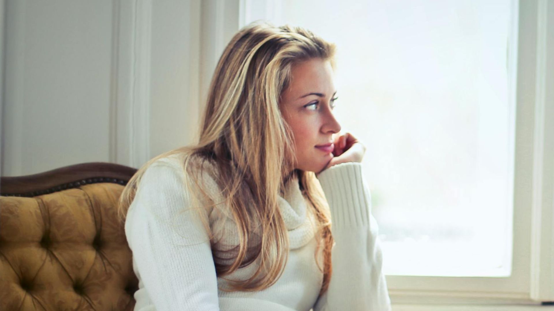 Young woman in a cozy armchair by a window, enjoying peaceful relaxation at home.