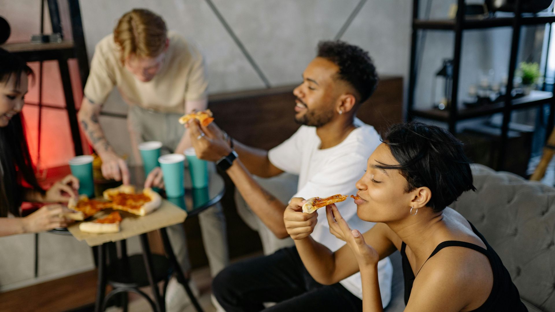 A diverse group of friends enjoying a pizza party indoors, smiling and relaxed.