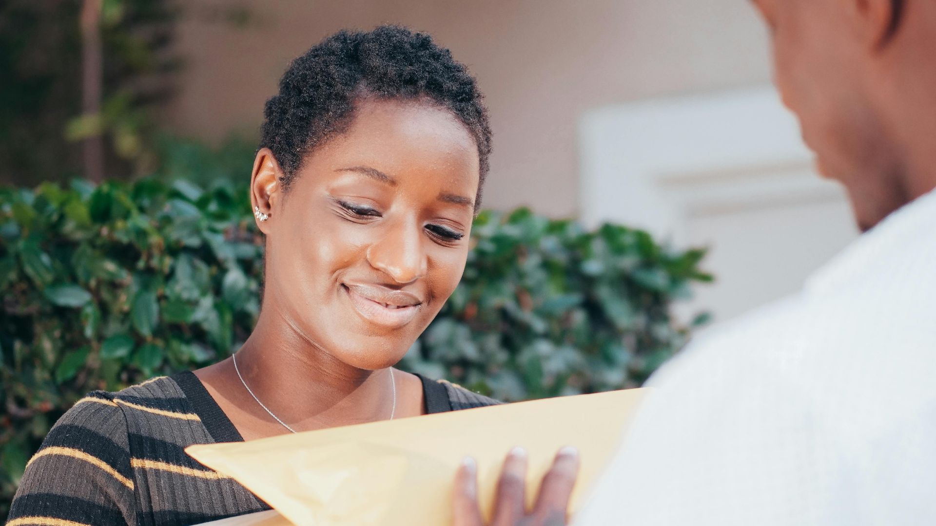 Smiling woman receiving a package from a courier in an outdoor setting.