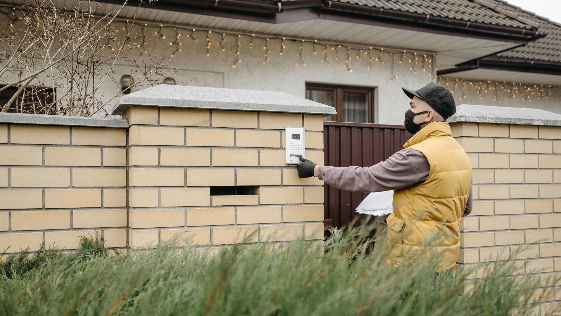 A delivery worker wearing a face mask presses a doorbell at a residential home, emphasizing contactless service.
