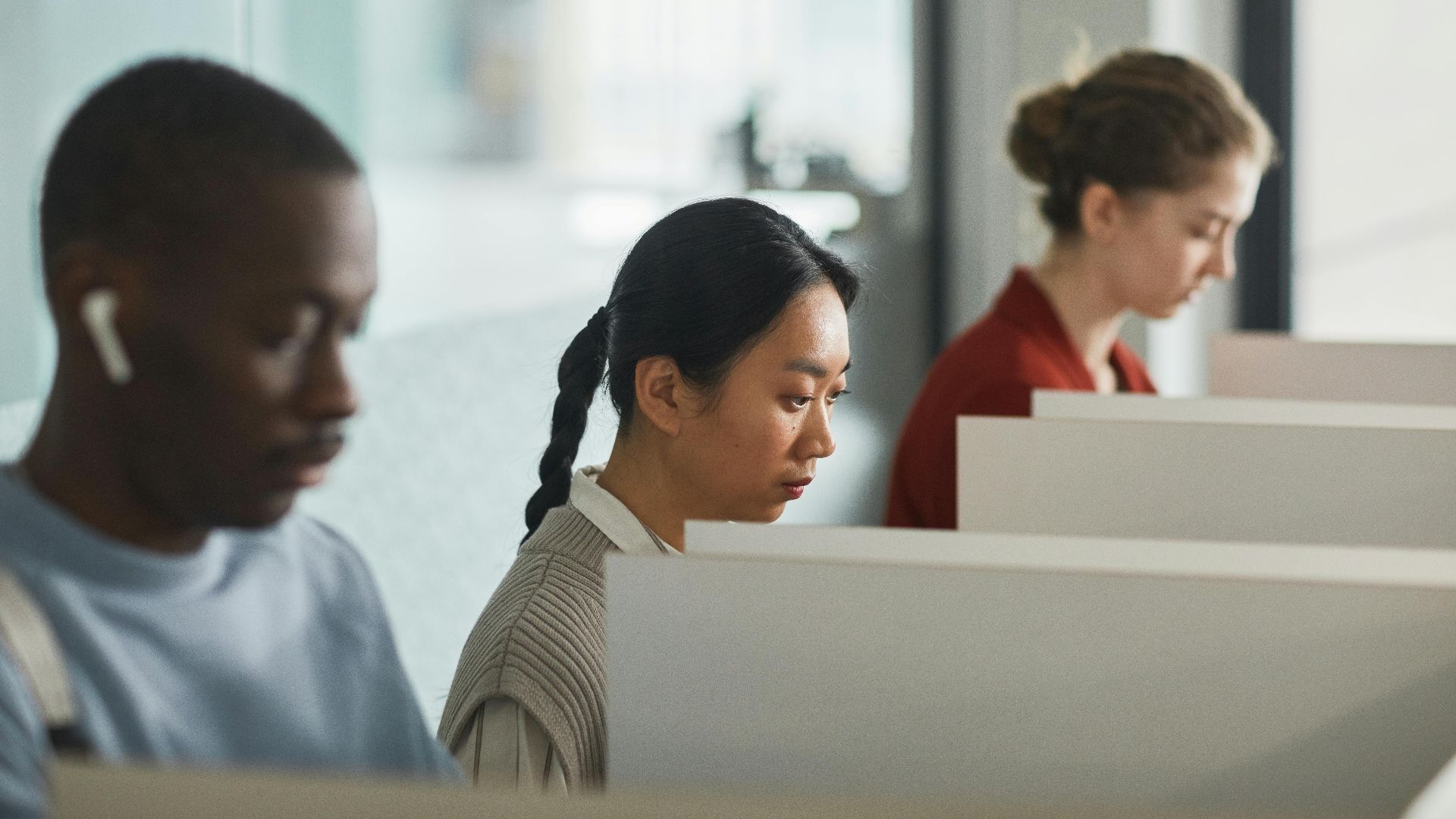 Employees working in cubicles using technology, showcasing a diverse and focused office environment.