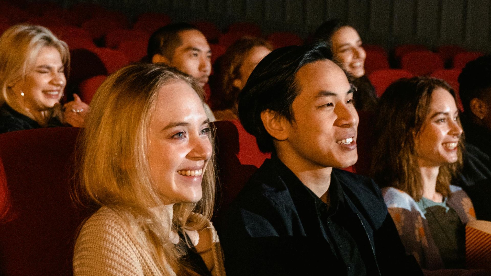 A diverse group of friends enjoying a movie at the cinema, with smiles and popcorn.