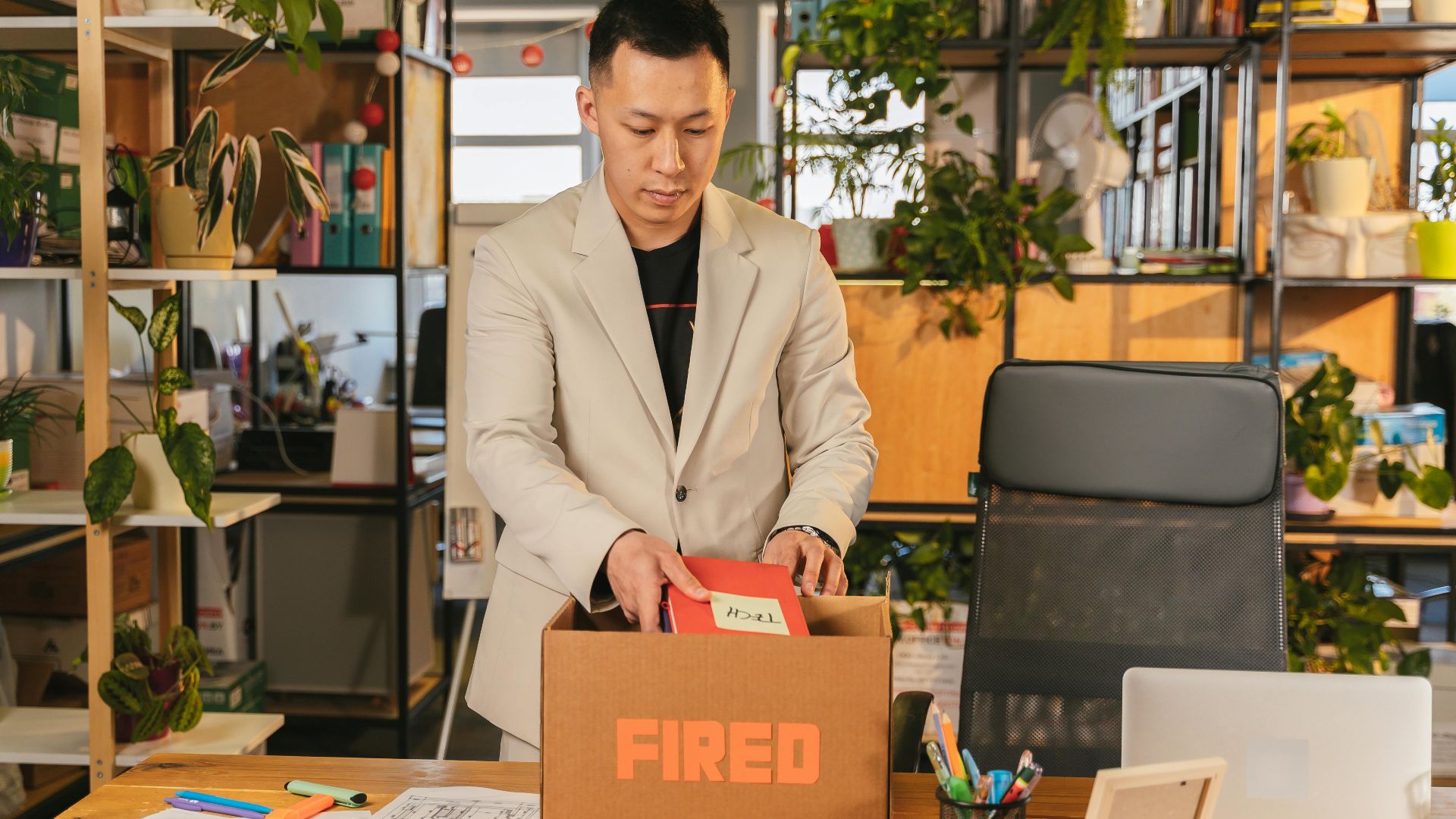 An adult man pack personal items after receiving a fired notice in an office setting, expressing corporate life challenges.