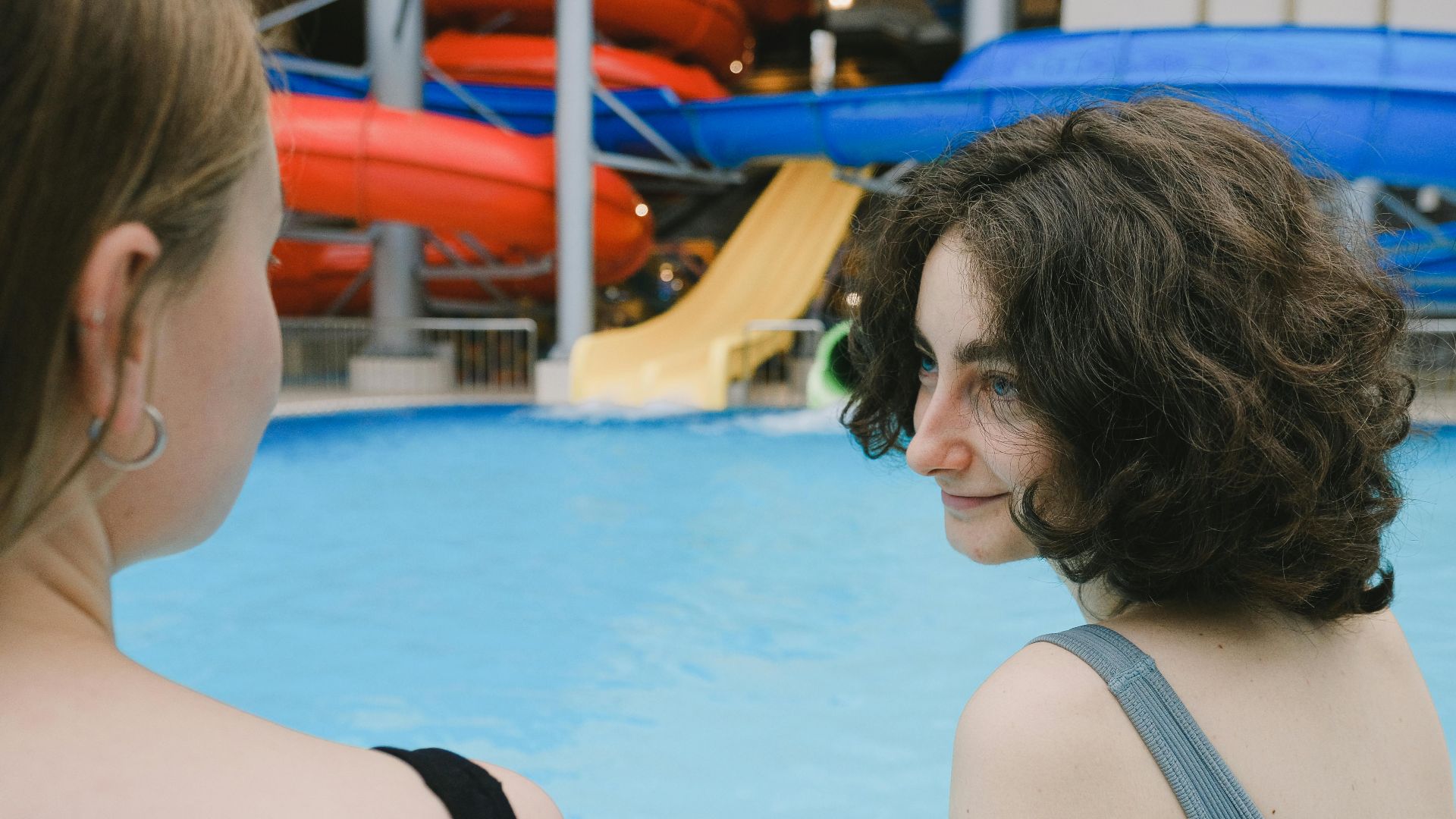 Two women enjoying leisure time next to a swimming pool surrounded by colorful water slides.