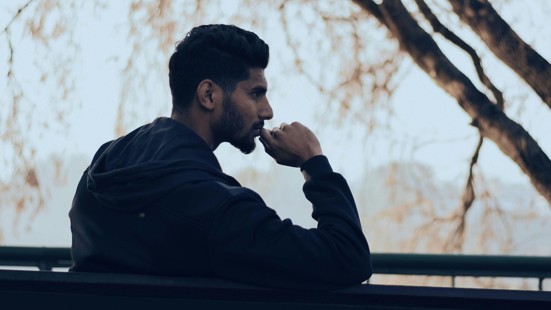 Man in deep thought sitting on a bench in a serene autumn park setting.