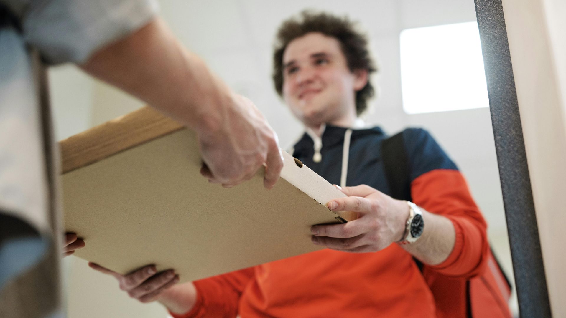 Smiling deliveryman handing over pizza box indoors, offering service.