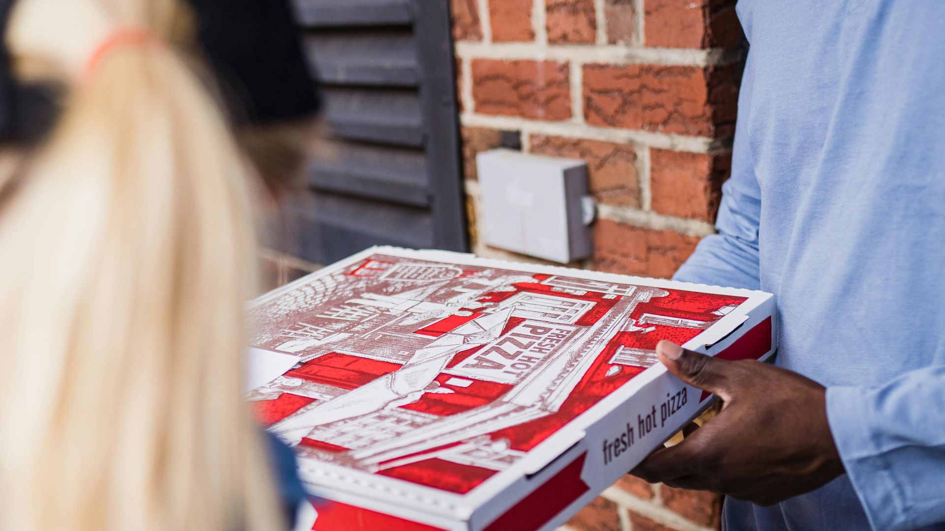 A delivery person hands a fresh pizza to a customer at the door, showcasing home delivery service.