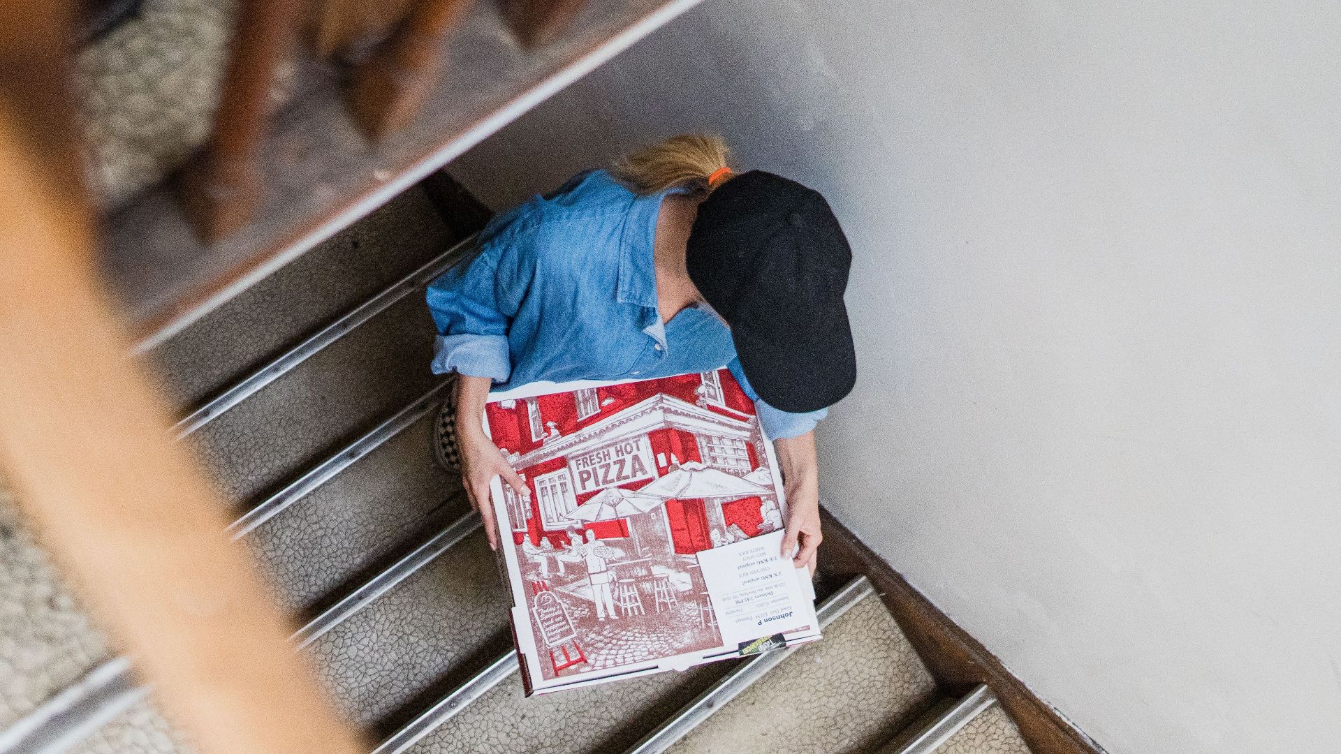 Overhead view of woman delivering pizza on stairs, highlighting delivery work.