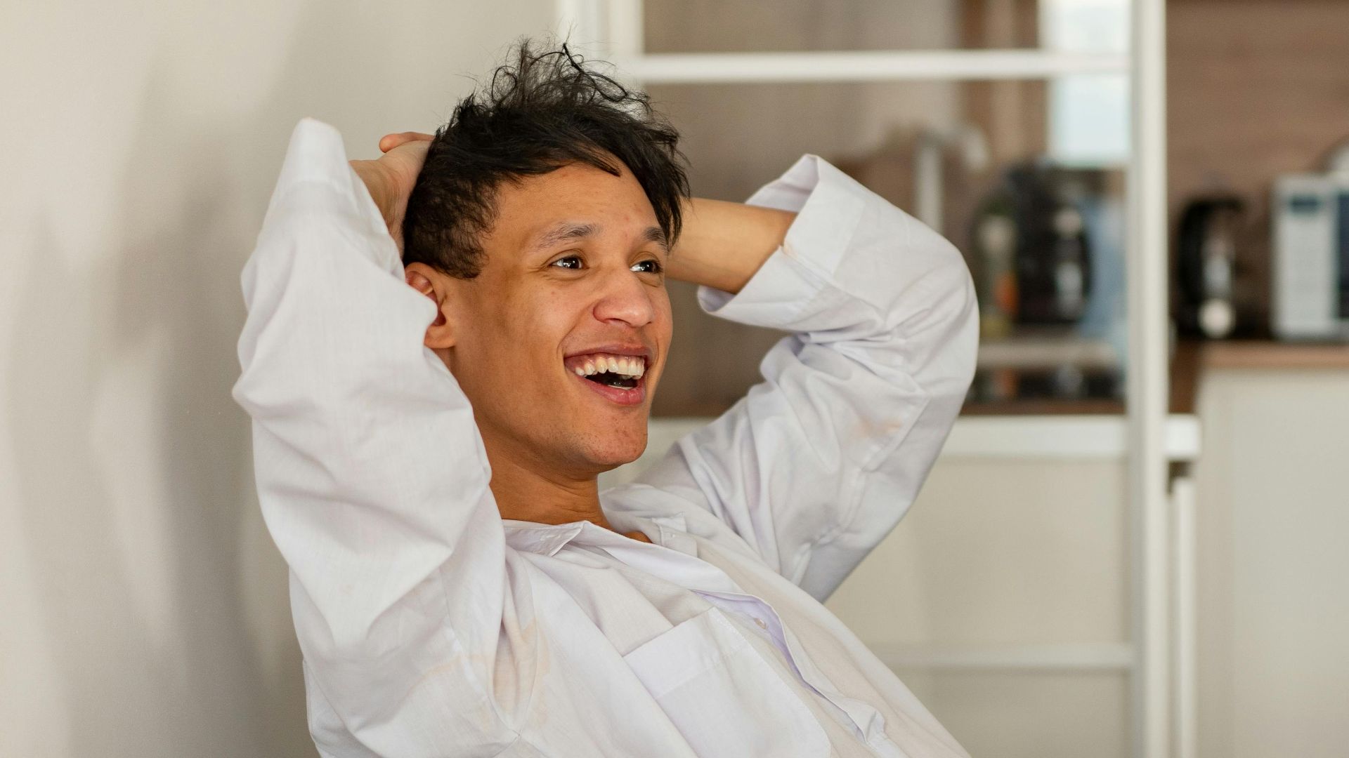 Casually dressed man enjoying leisure time at home with an open laptop, expressing happiness and relaxation.