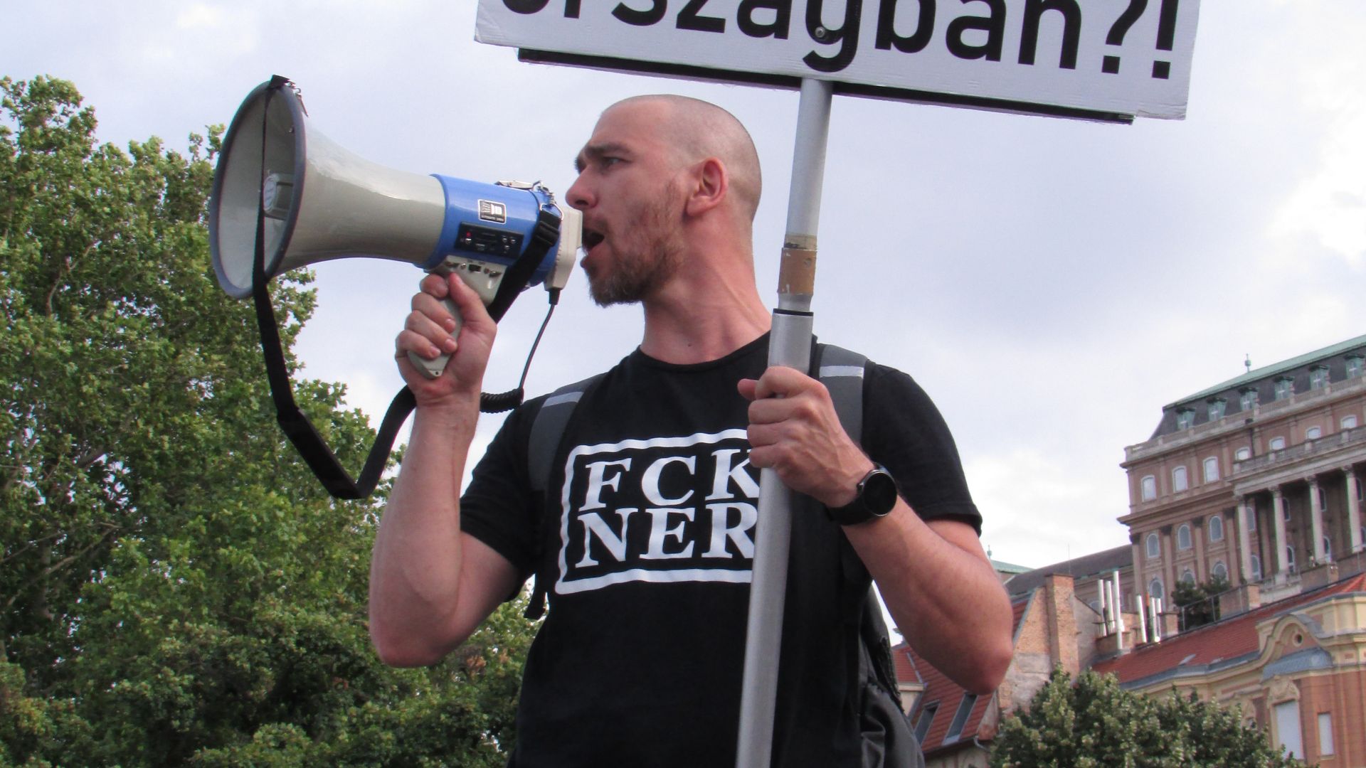 Protestor standing above the crowd with a megaphone and protest sign at the We Will Not Stop! protest on 2025 July 29