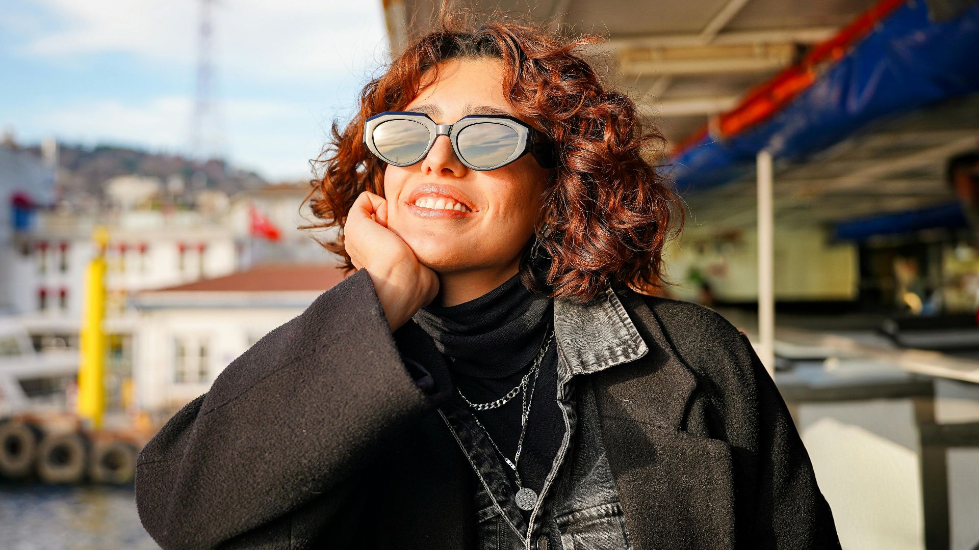 Woman enjoying a sunny day on a ferry, wearing sunglasses and a black outfit.