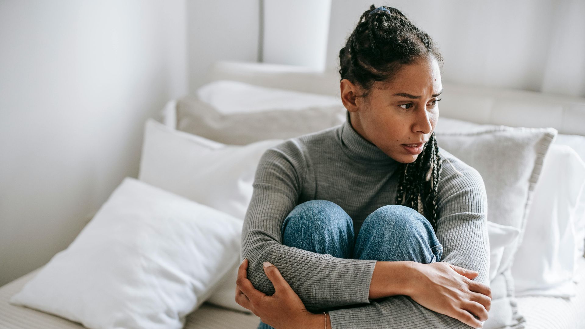 Frustrated distressed ethnic female thinking on problem while sitting on bed and looking away