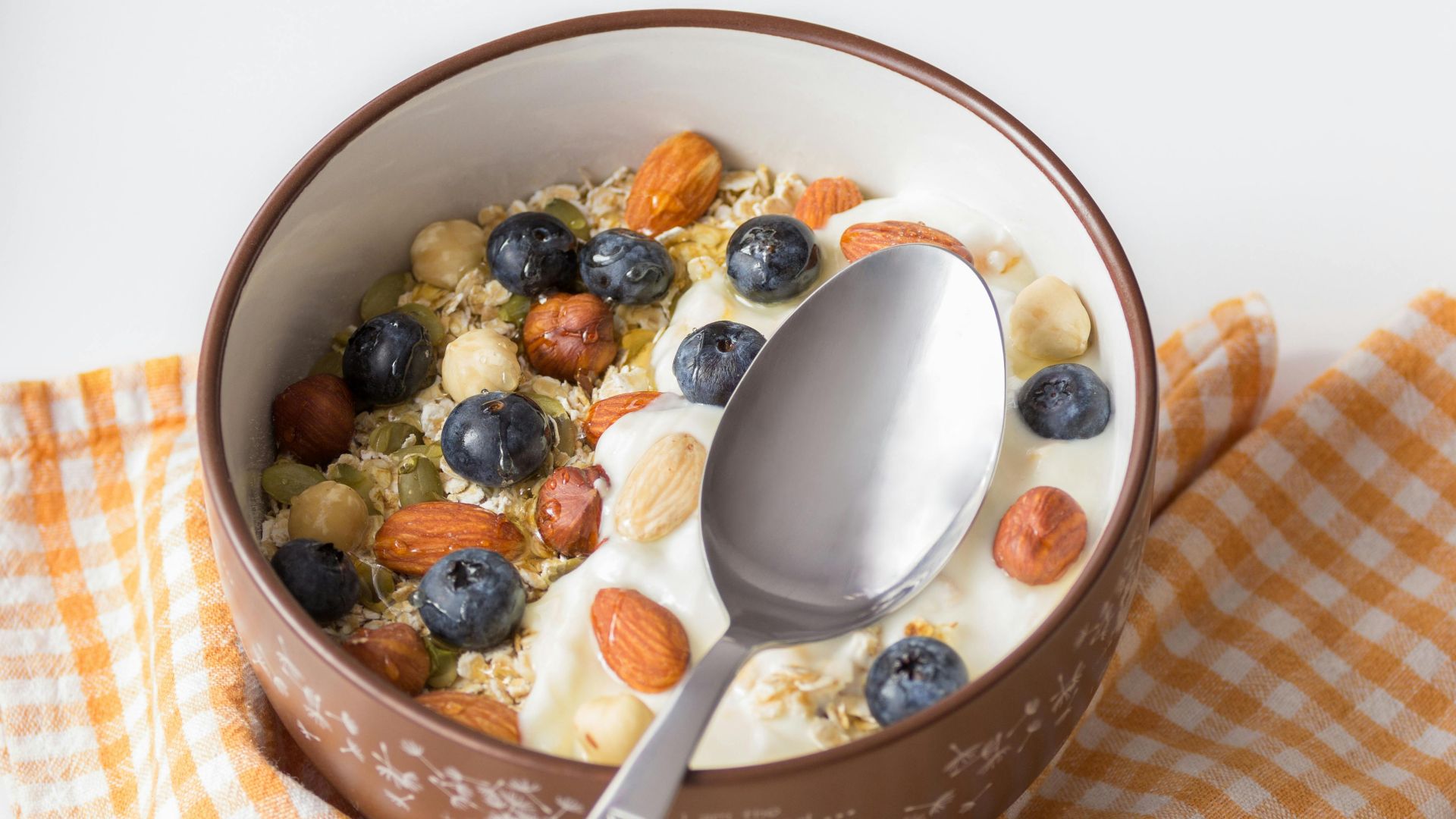 A delicious breakfast bowl featuring yogurt, nuts, and fresh blueberries on a checkered cloth.
