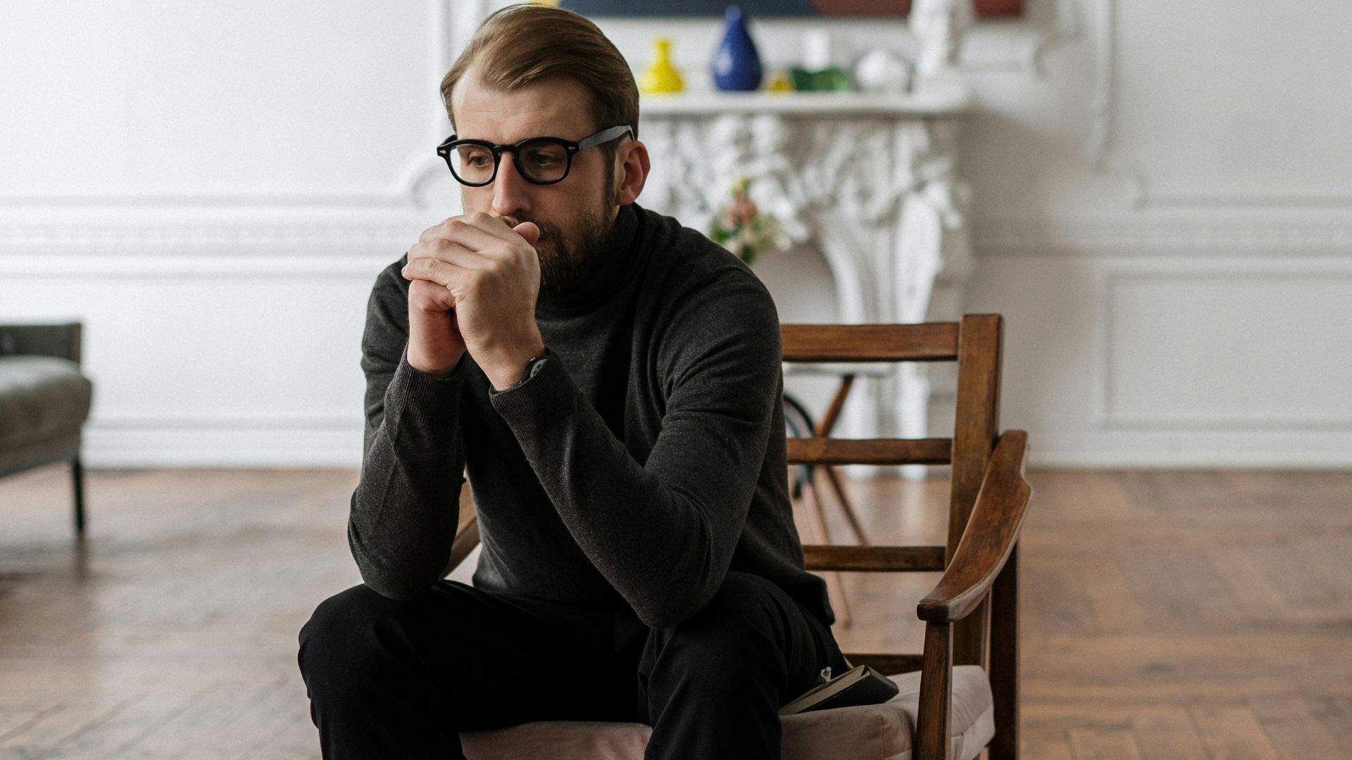Man sitting in a stylish indoor setting, contemplating thoughts.
