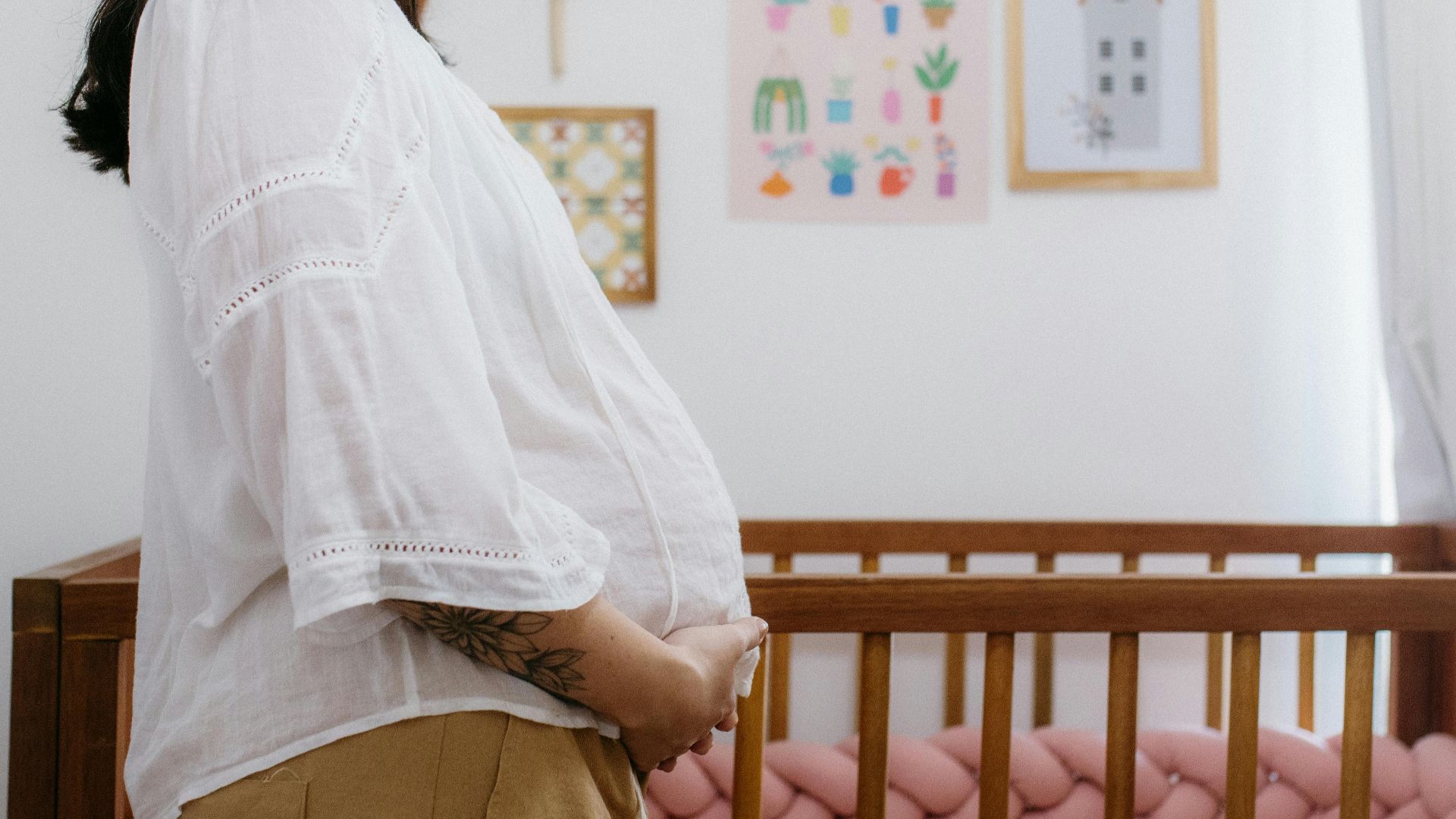 Expectant mother standing beside a wooden crib in a beautifully decorated nursery room.