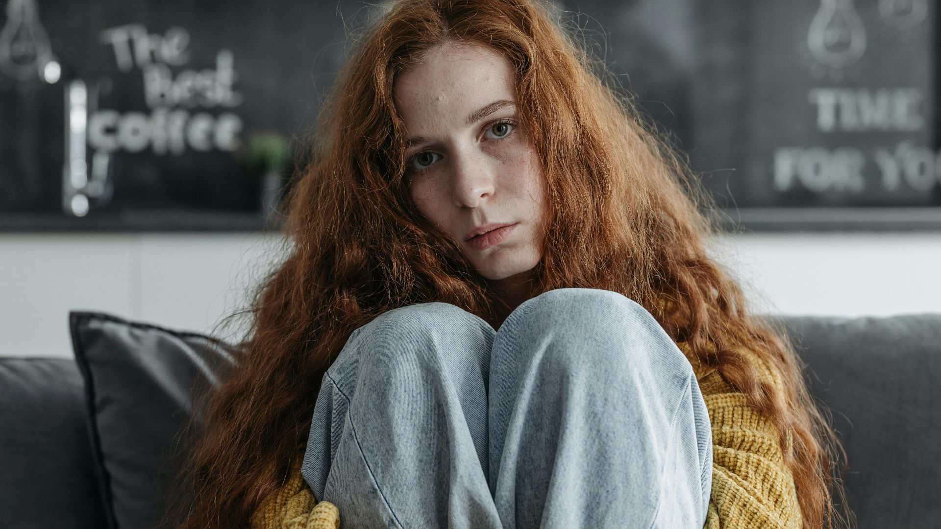 Young woman with red hair sitting indoors, expressing introspective emotion.