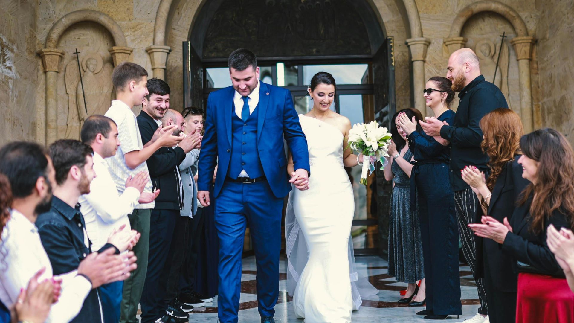 Bride and groom exiting a church, surrounded by applauding guests in an outdoor wedding ceremony.