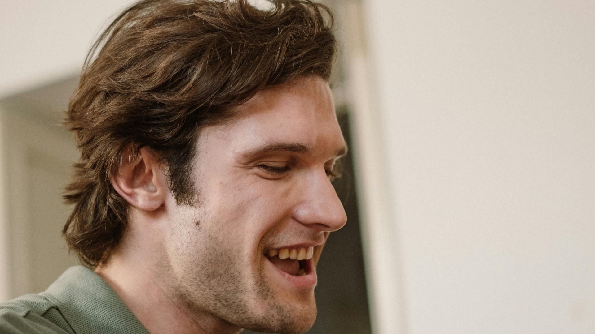 Side profile of a man smiling and appearing relaxed indoors in a casual setting.