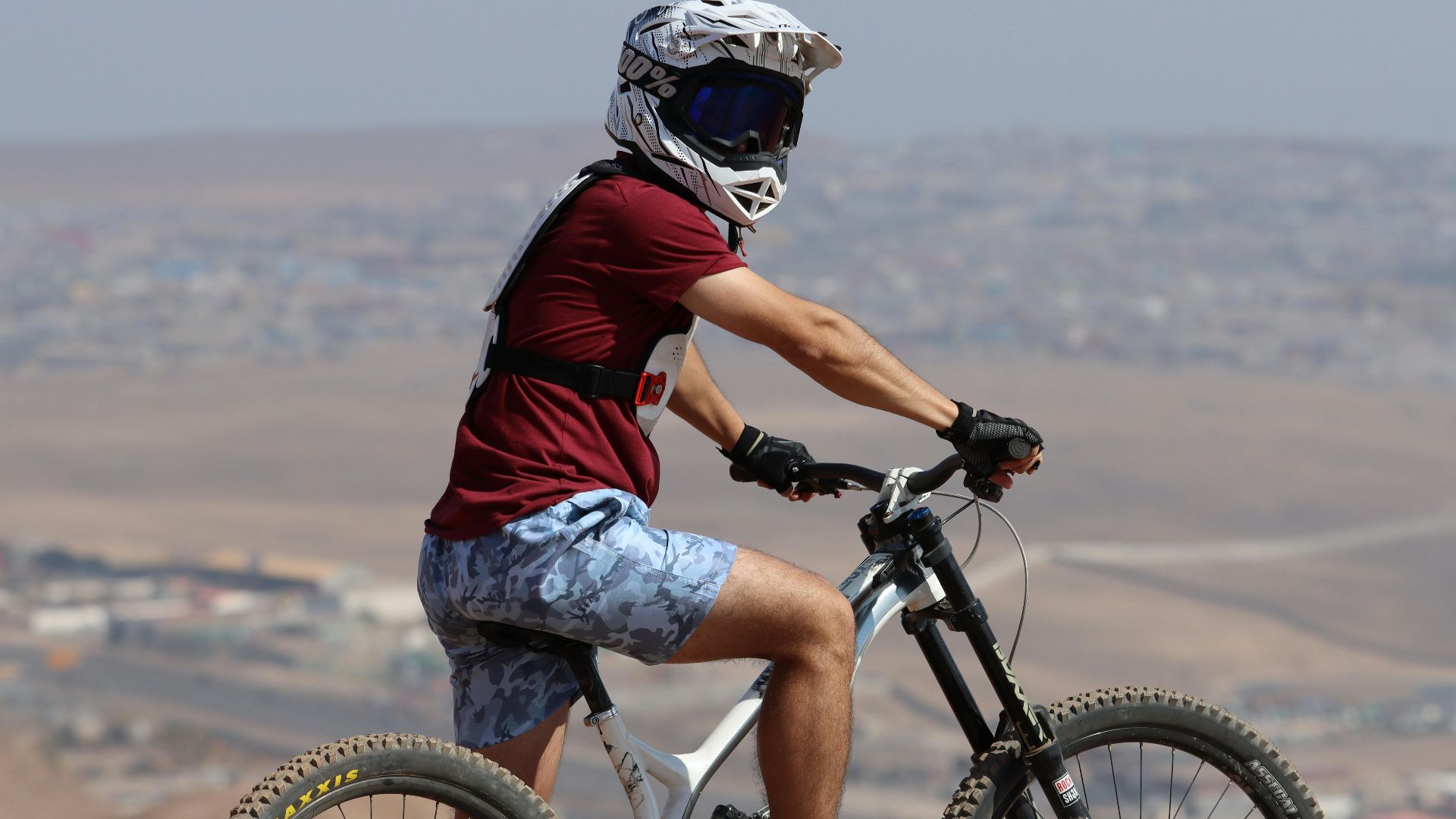 Man wearing helmet and goggles rides a mountain bike in a desert area, showcasing adventure and sportsmanship.