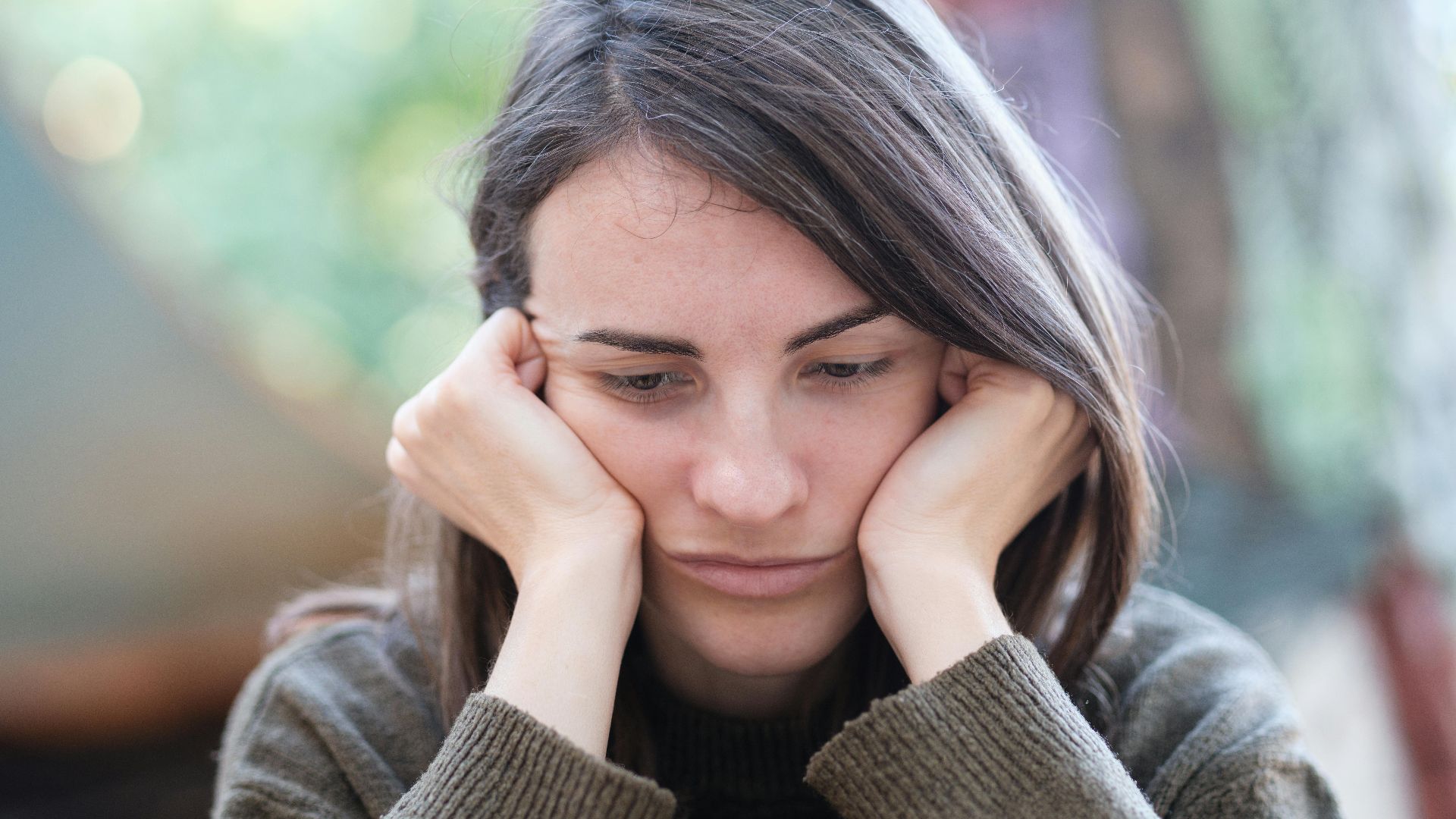 Portrait of a young woman looking pensive and thoughtful while sitting outdoors.