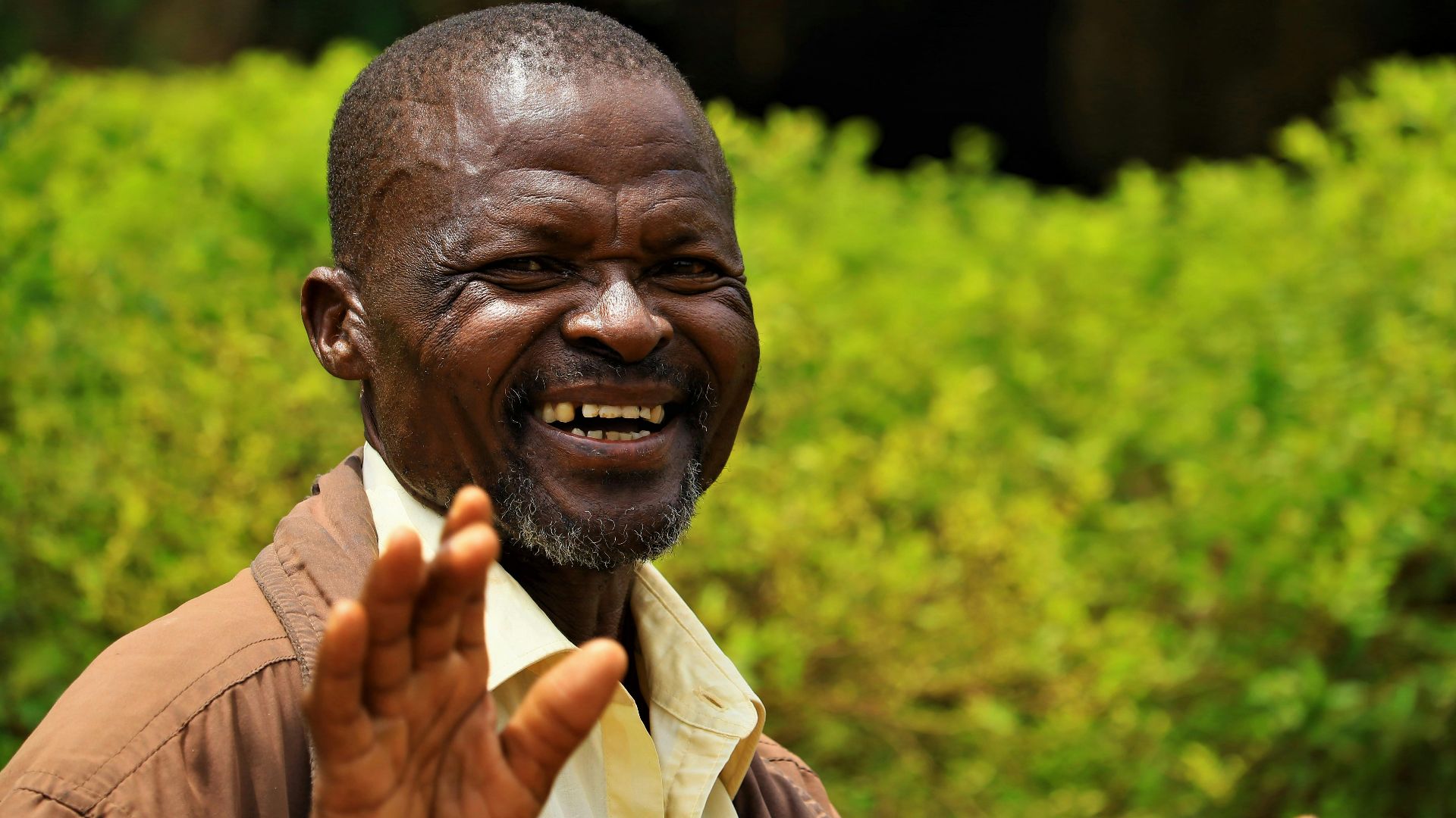 African man smiling joyfully in a vibrant green outdoor setting in Uganda.