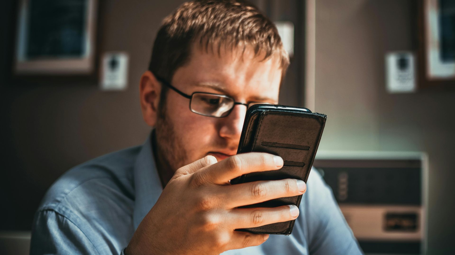 Serious businessman wearing glasses focused on smartphone in a modern office setting.