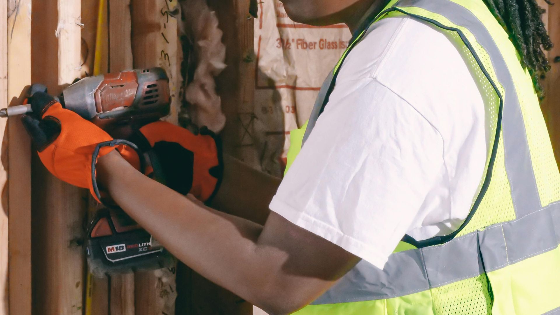 Black woman using a drill on site wearing PPE including hardhat and gloves.