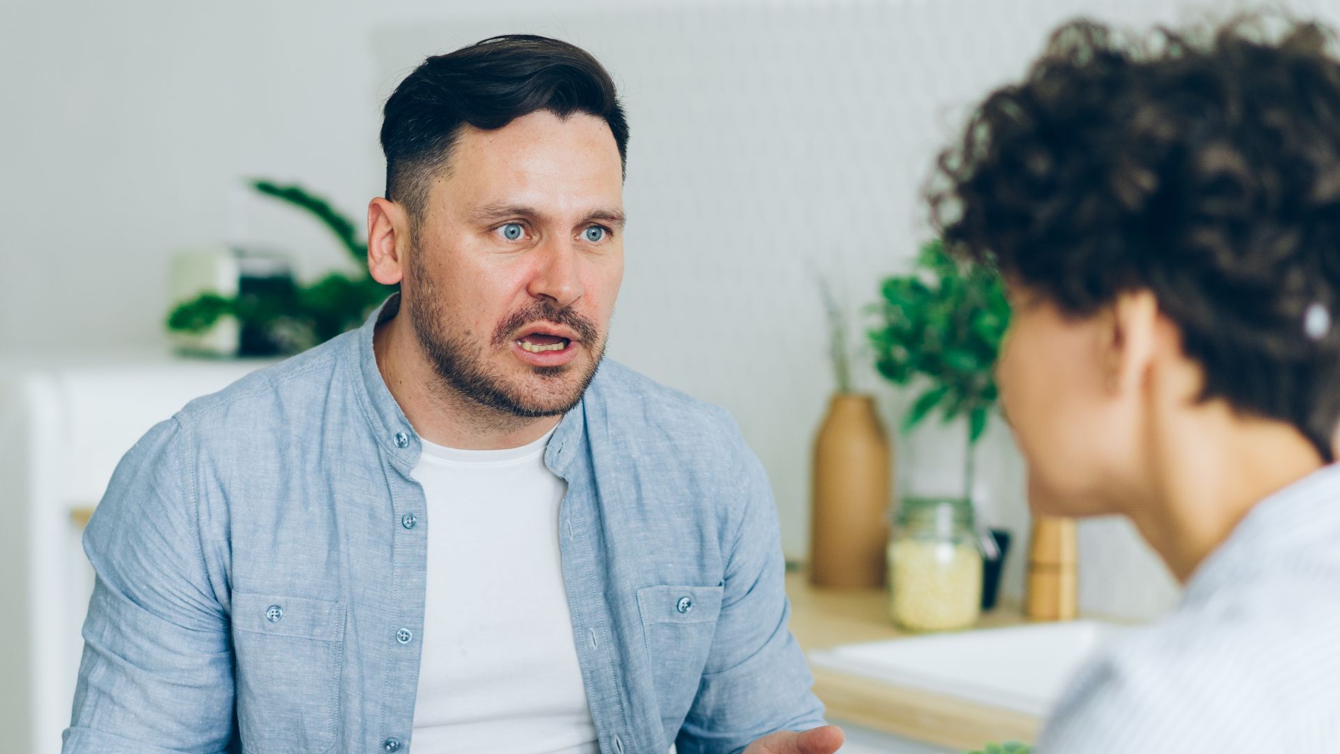 Couple having a serious conversation at the kitchen table with coffee cups.