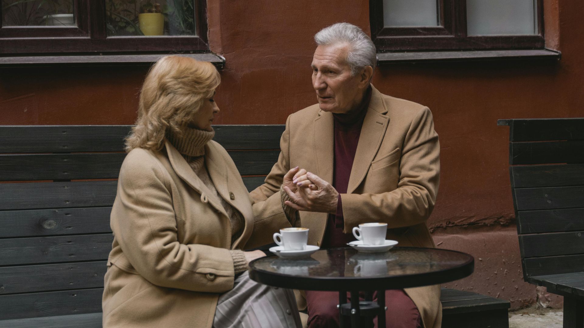 An elderly couple enjoys a conversation over coffee at an outdoor cafe.