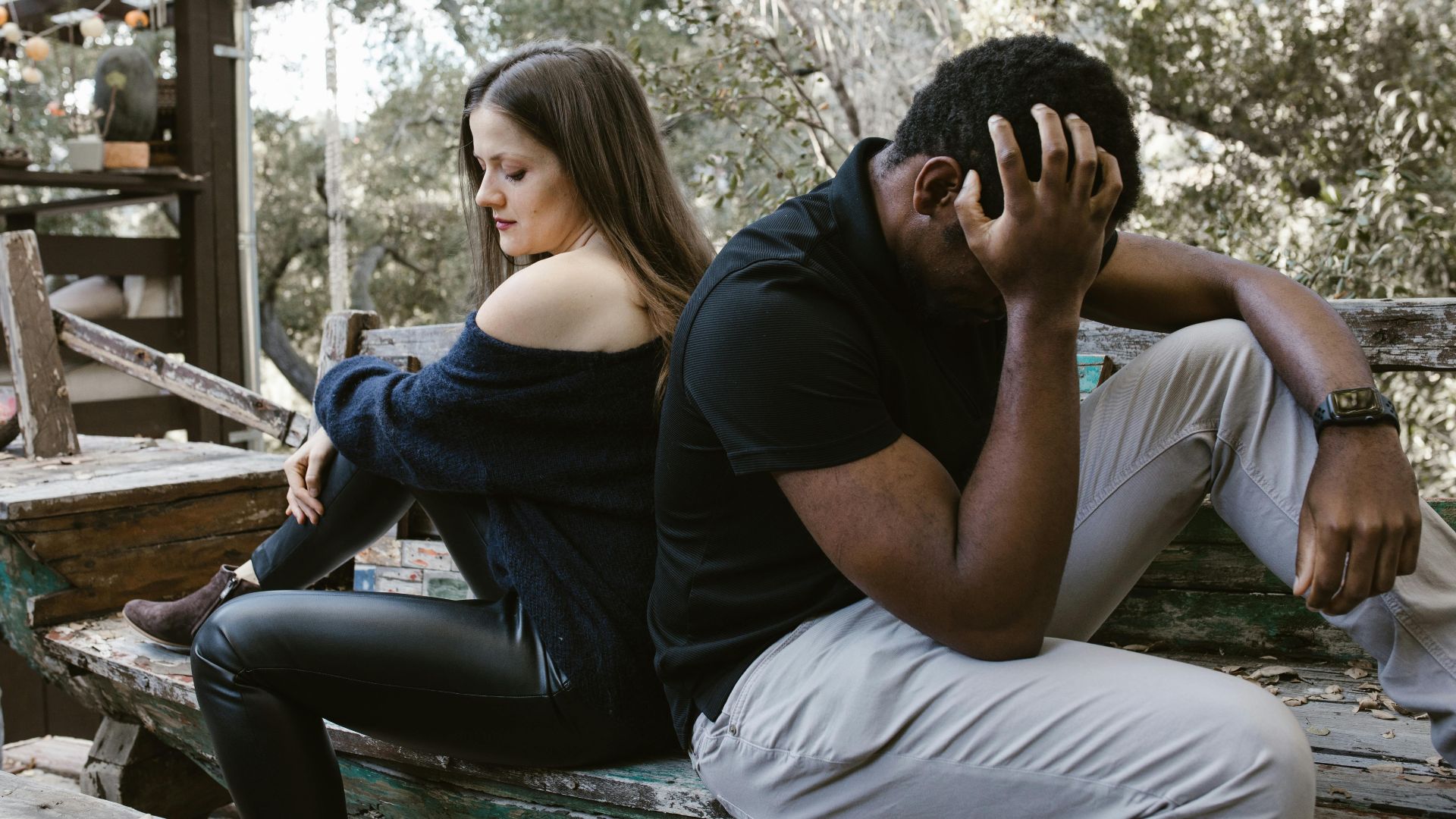 A couple sits back to back on a bench, depicting emotional conflict and loneliness.