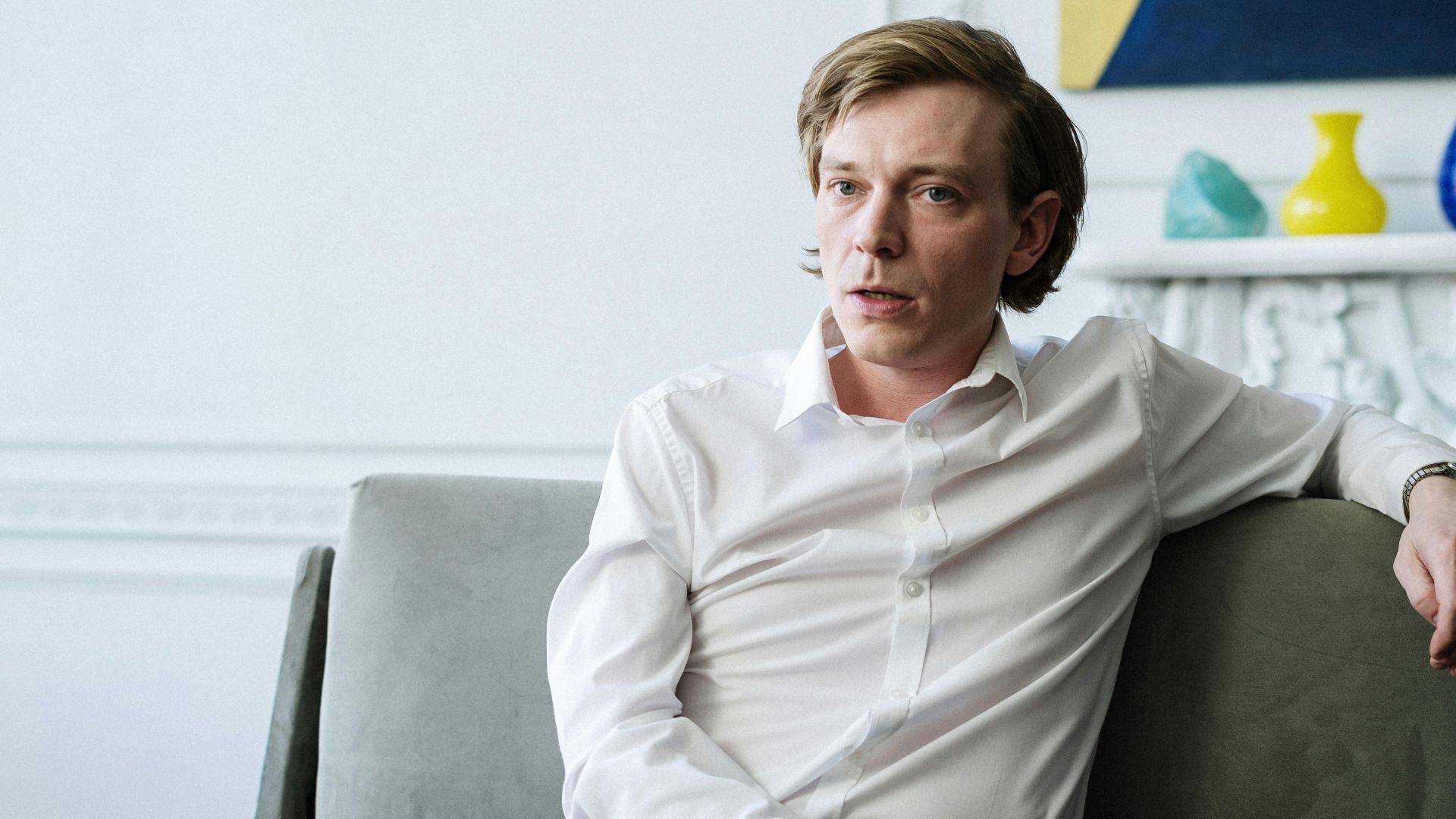 Confident man in white shirt sitting on sofa, representing consulting or therapy session indoors.