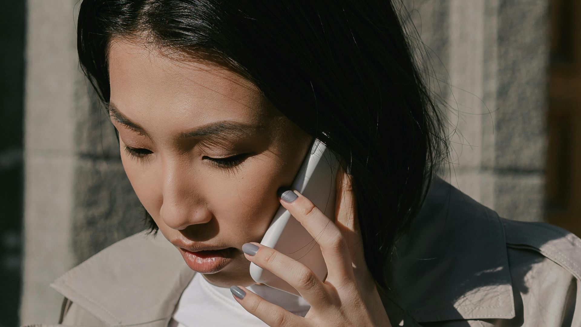 Professional woman in a trench coat talking on her cellphone while standing outside.