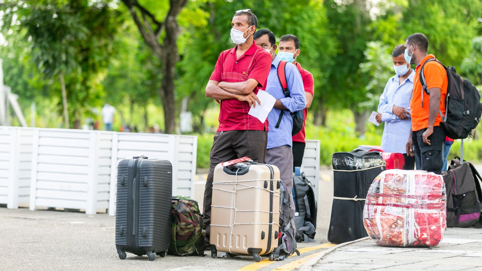 People standing with suitcases wearing masks outdoors, indicative of travel during COVID-19 times.
