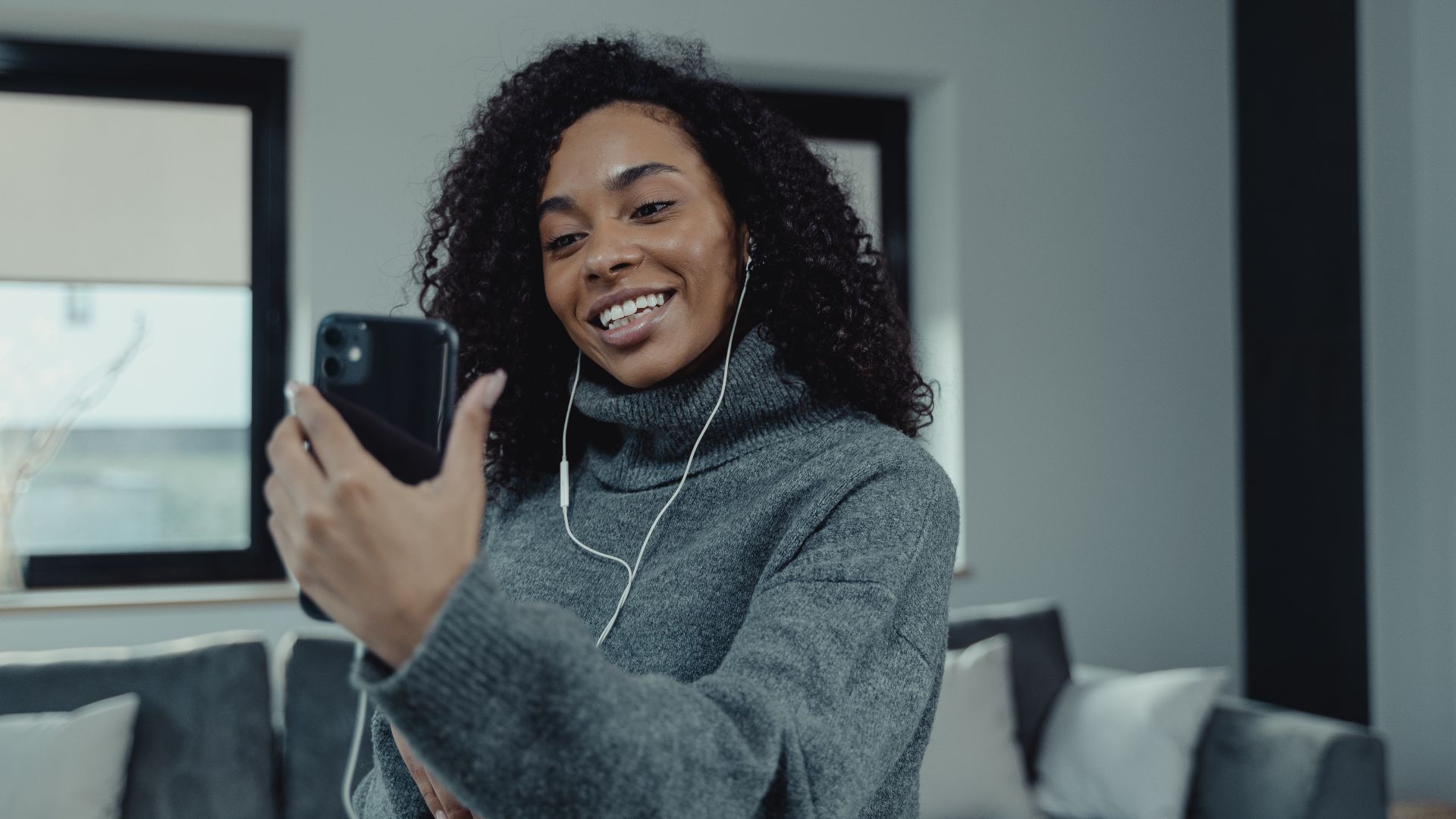 A cheerful woman with curly hair making a video call in a cozy living room.