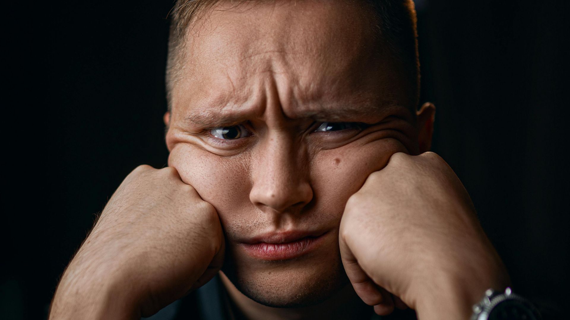 Unhappy male in formal outfit with wristwatch leaning on fists while looking at camera
