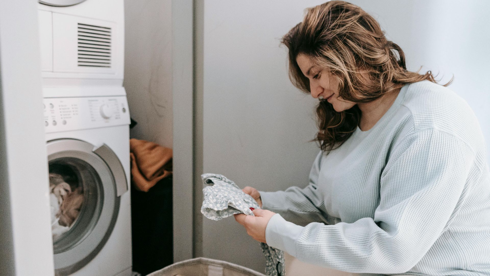 Woman organizing laundry in a laundry room with a washing machine.