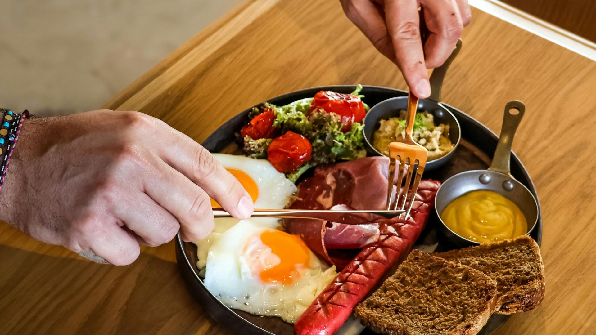 Enjoy a hearty breakfast with eggs, sausages, and fresh vegetables on a wooden table.