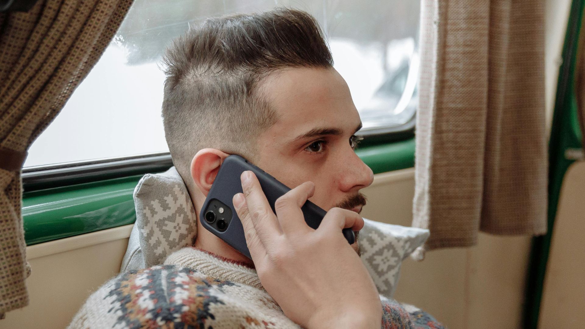 Casual adult man wearing sweater, relaxing indoors while talking on phone.