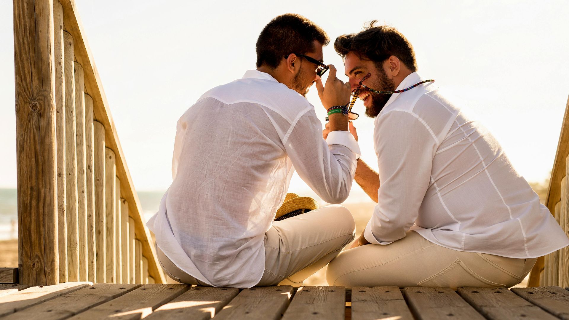 A joyful couple enjoys a sunny day on a wooden deck by the beach, capturing happiness and togetherness.