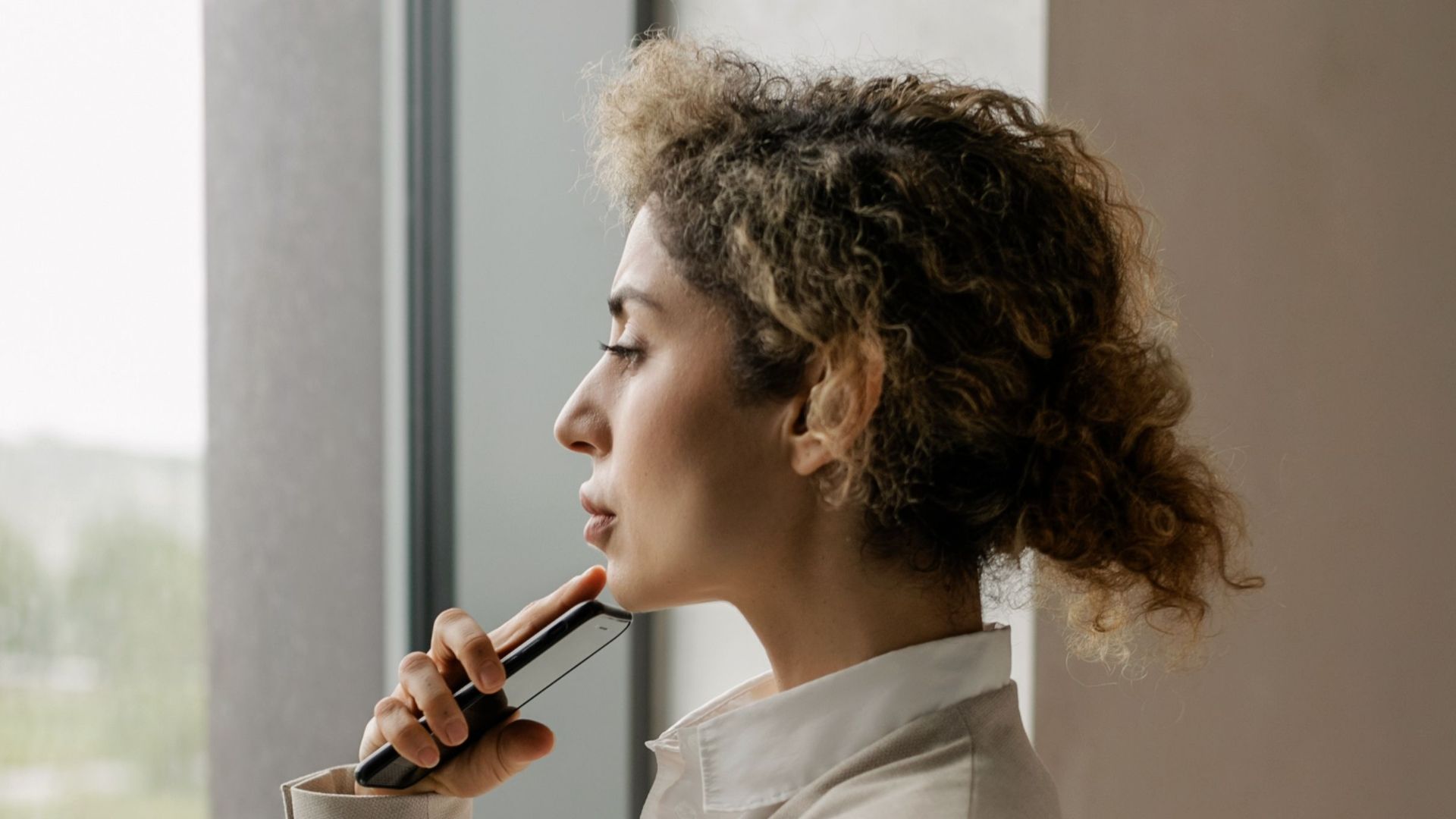 Professional woman in suit looking thoughtfully out a glass window, suggesting corporate environment.