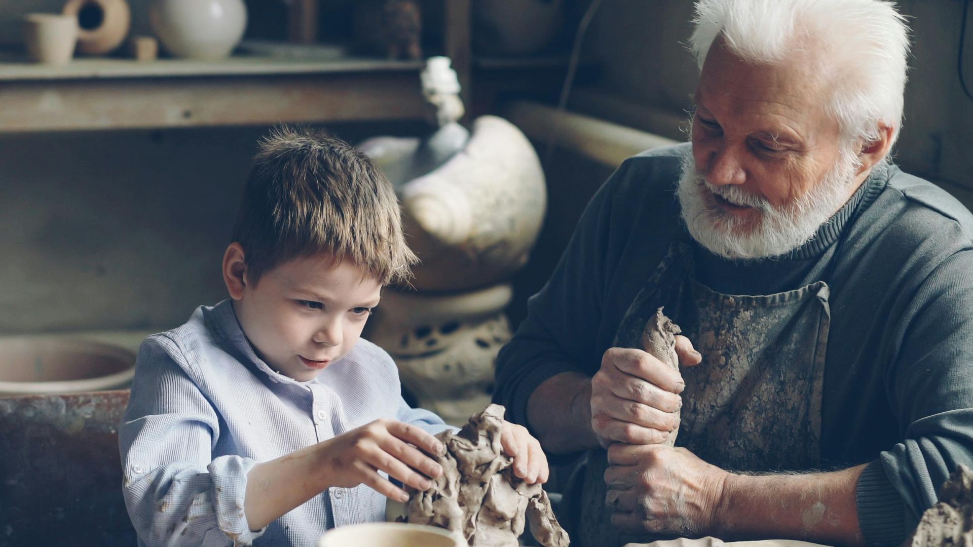 A grandfather and grandson bond while creating pottery together in a cozy workshop.