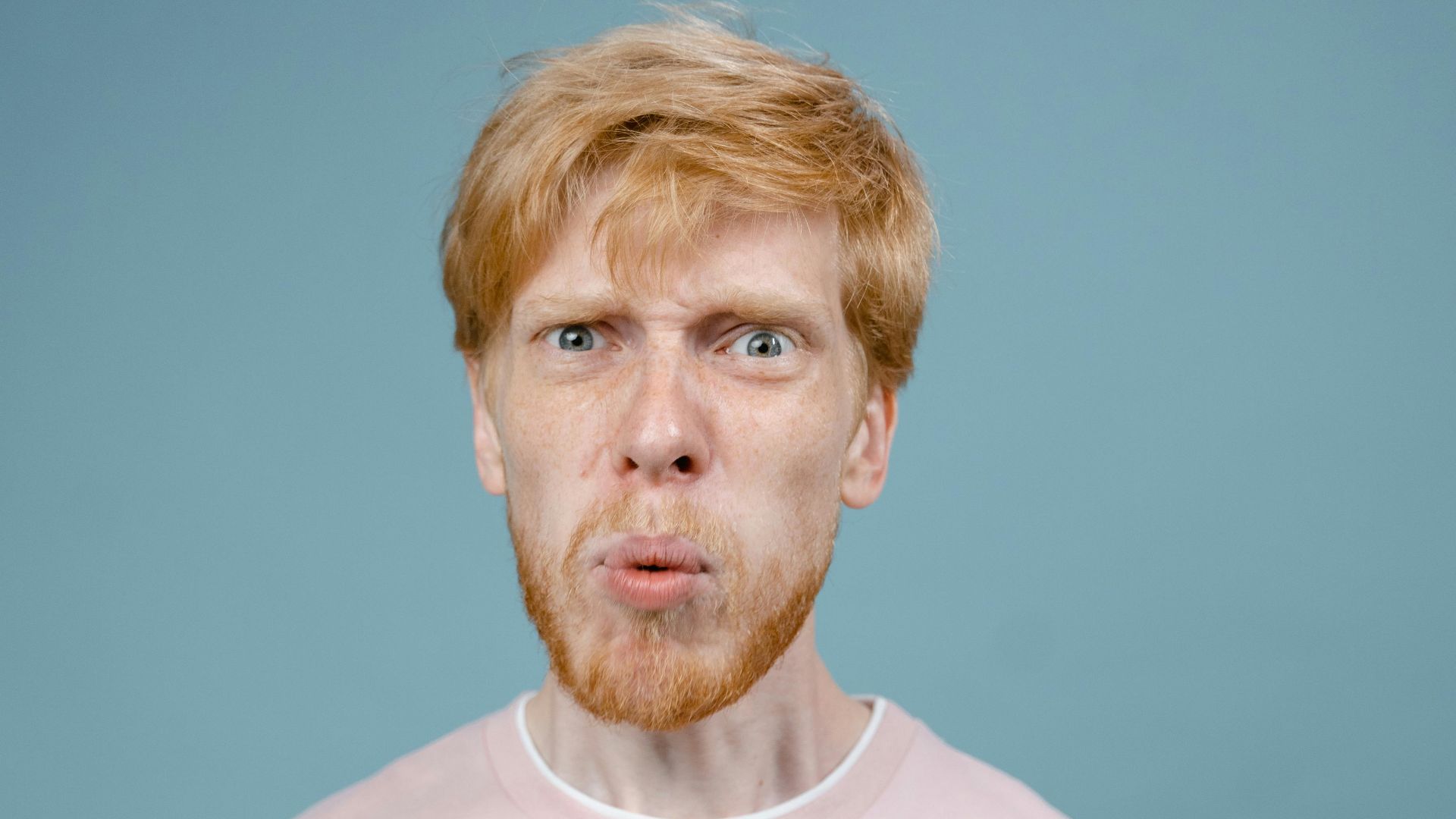 Adult man with angry facial expression in pink shirt, studio shot with blue background.
